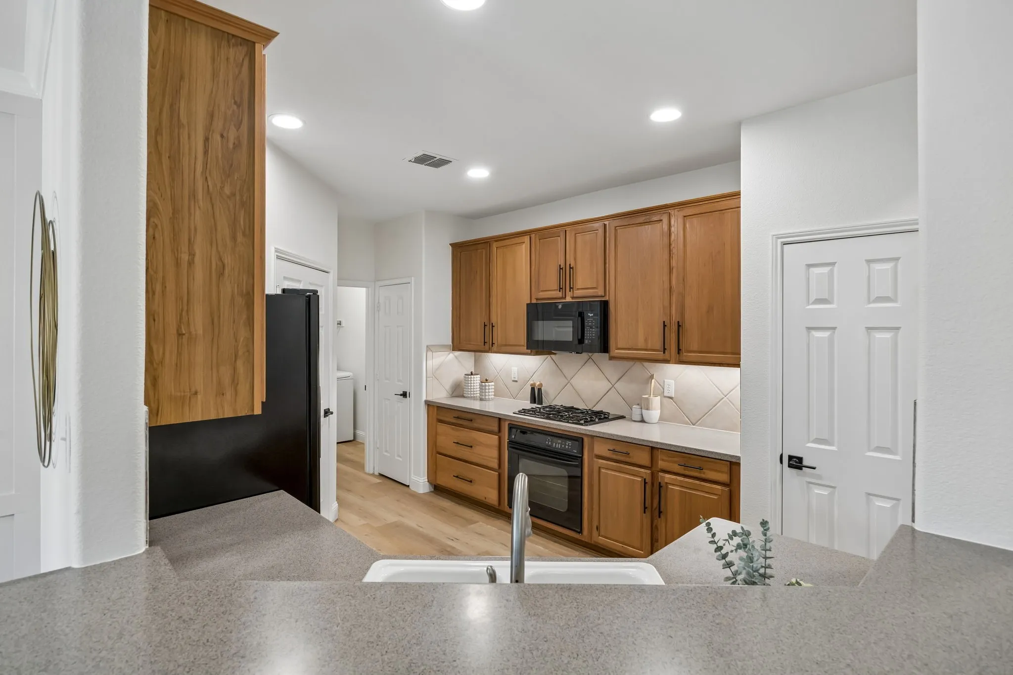 Kitchen featuring wood-finish cabinetry, light-toned countertops, and a diagonal tile backsplash