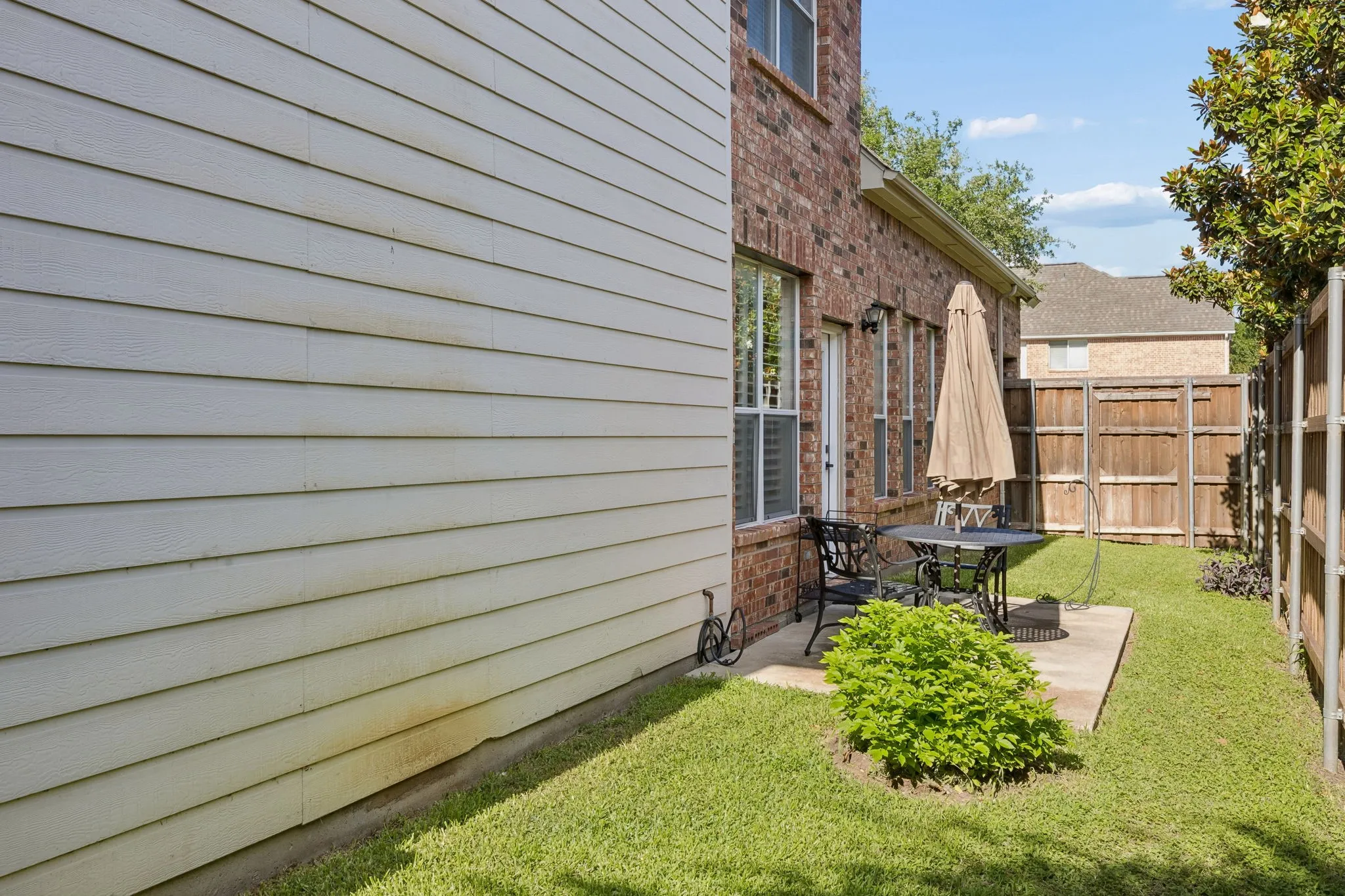 Private outdoor patio area featuring a concrete slab, surrounding green lawn, and a partial brick exterior