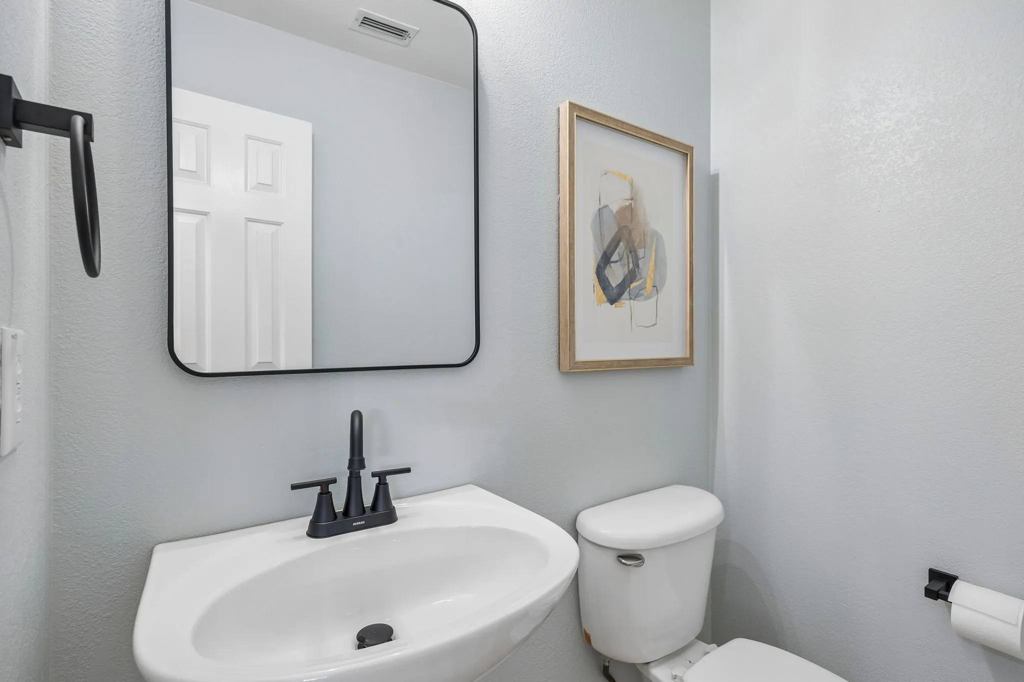 Pedestal sink with a matte black faucet, complemented by a rectangular mirror with a black frame