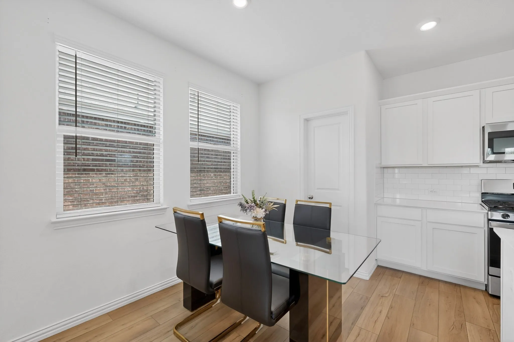Modern kitchen dining area featuring light wood-finish flooring, white cabinetry, a white subway tile backsplash, and stainless steel appliances