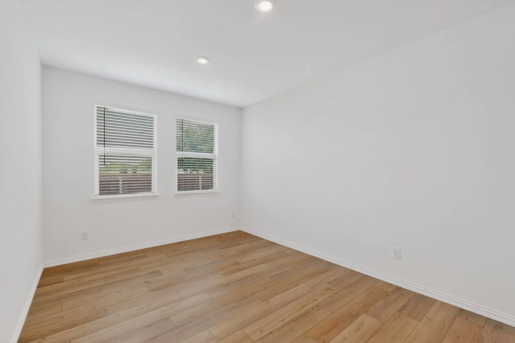 Bright room featuring two windows with horizontal blinds, wood-finish flooring, recessed lighting, and white baseboards