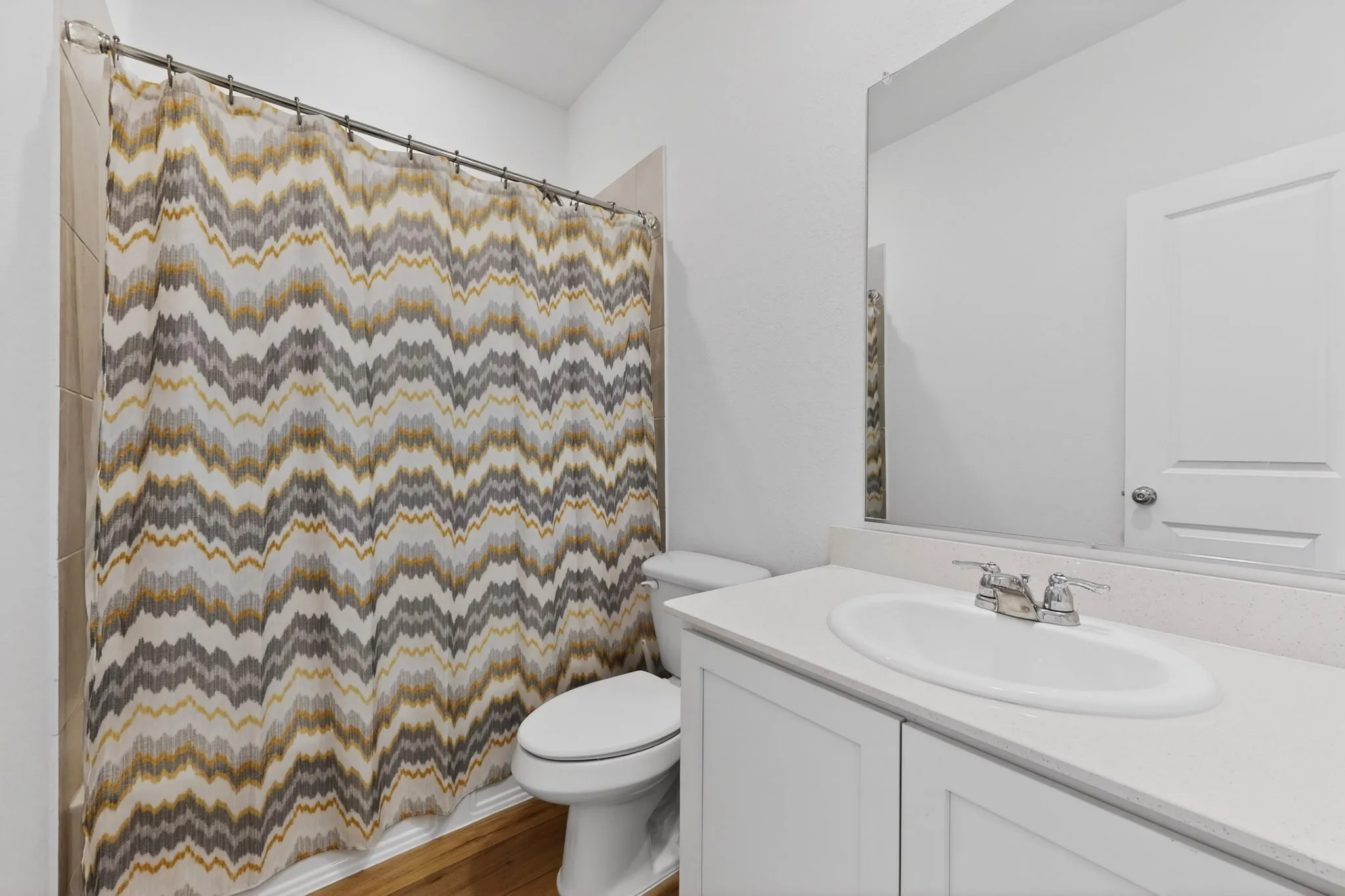Bathroom featuring a white vanity with an undermount sink, a large mirror, a toilet, and light-toned wall tile surrounding the shower area