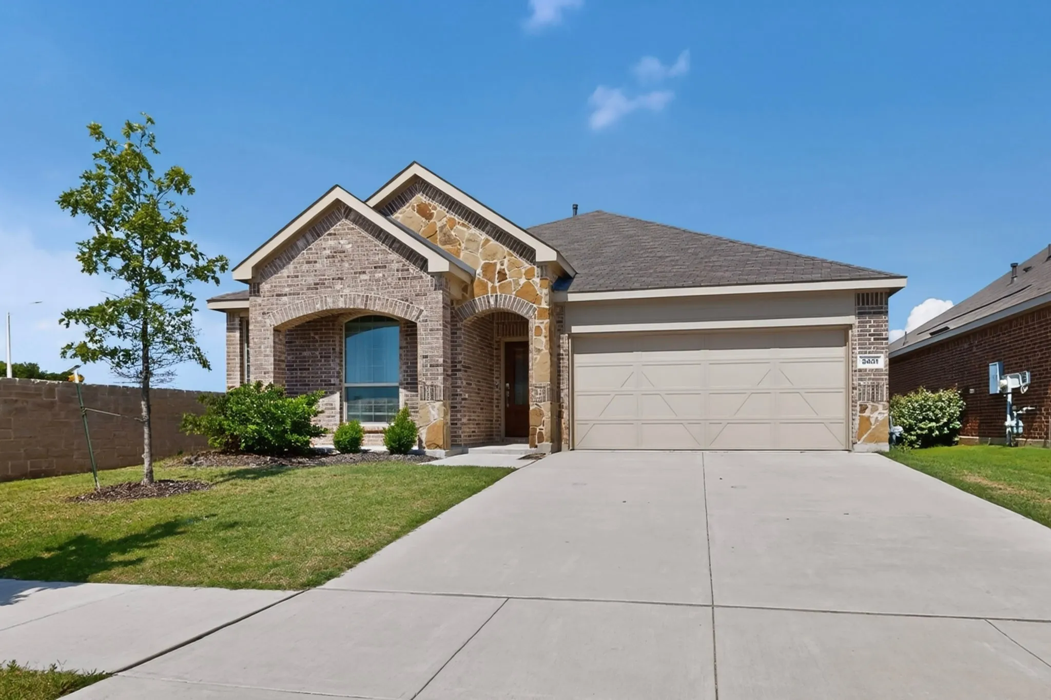 Exterior featuring brick and stone masonry, a pitched roof, an arched entry, a large front window, and an attached two-car garage