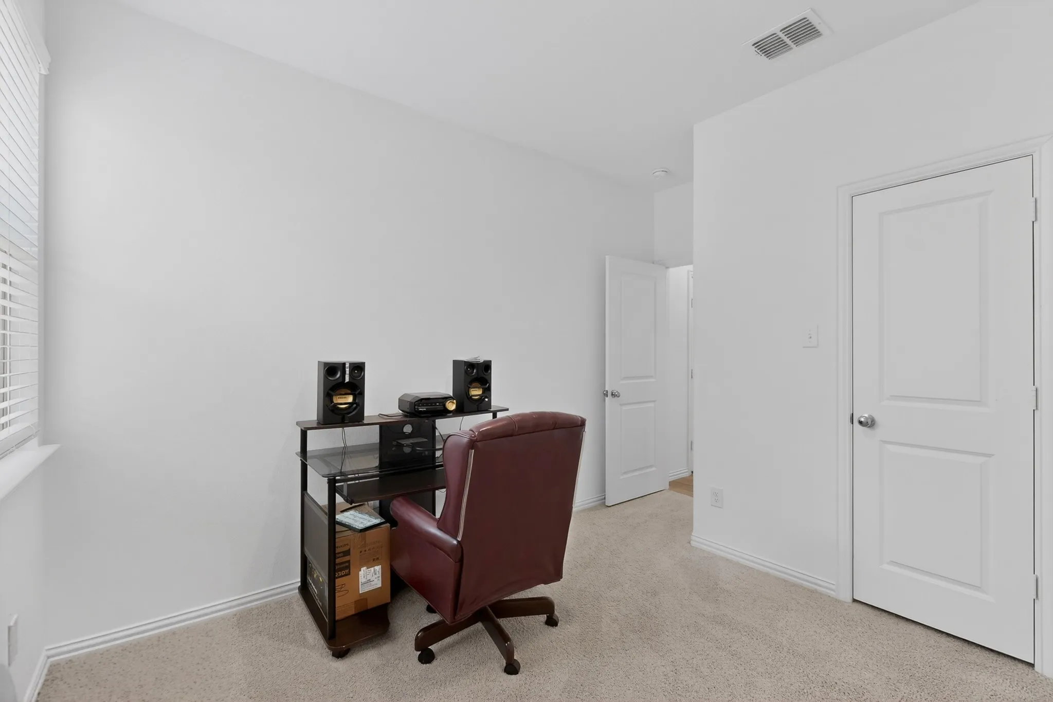 Bright room with neutral carpeting and white painted walls, featuring a window with horizontal blinds and two white paneled doors with chrome hardware
