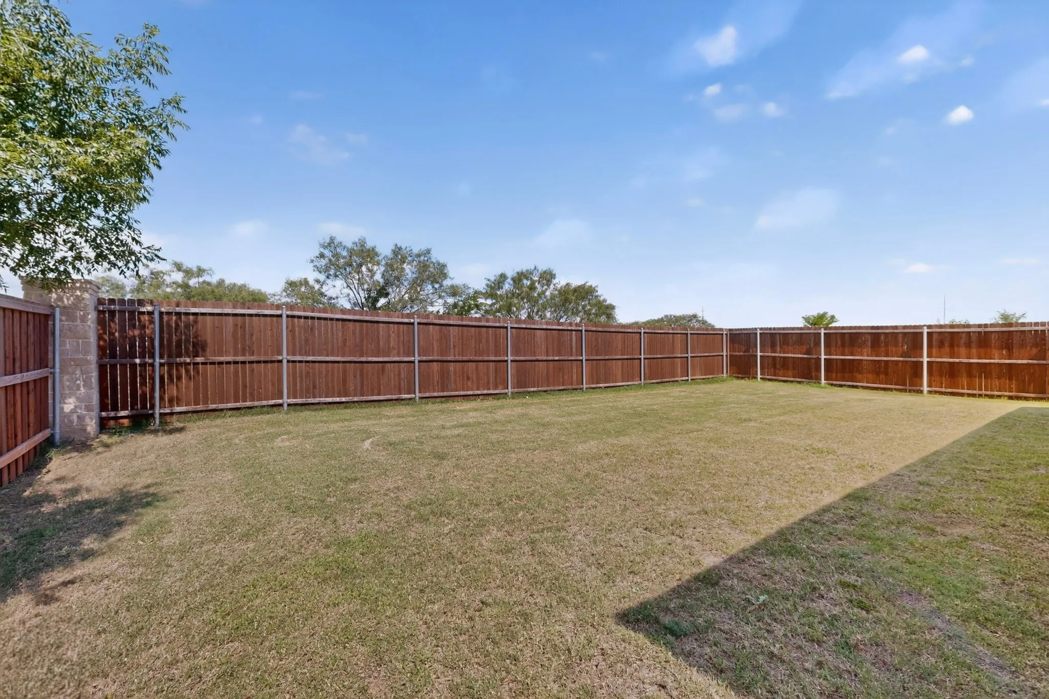 Expansive grassy yard featuring a wood privacy fence with metal posts and a concrete block column