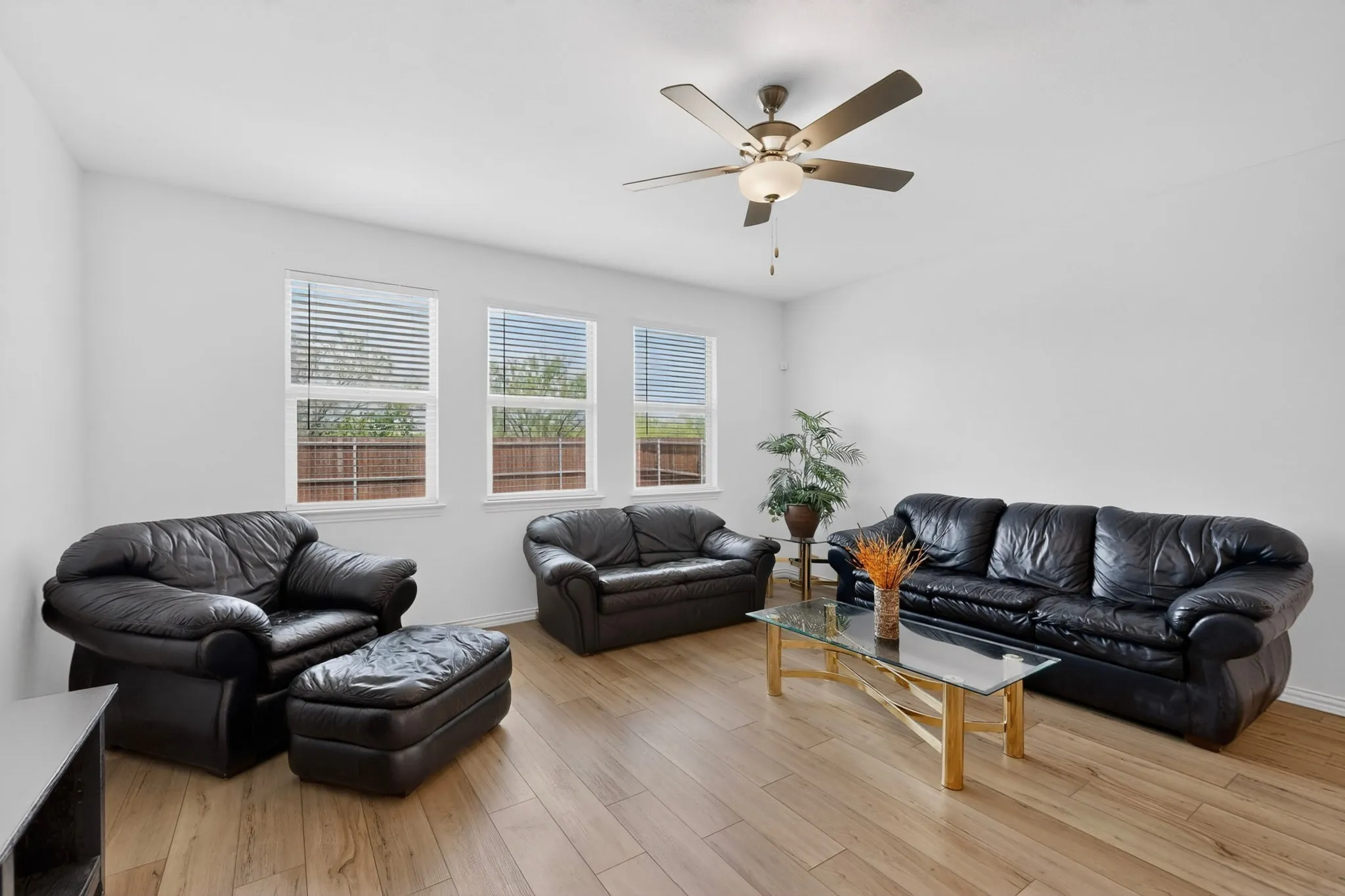 Bright living area featuring wood-finish flooring, white walls, and a ceiling fan with integrated lighting
