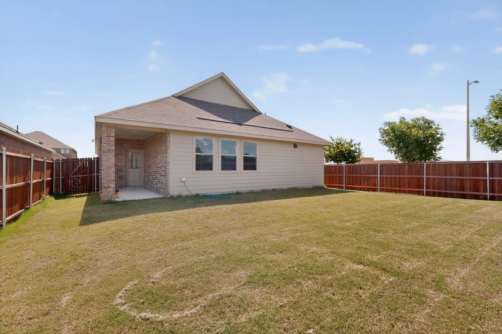 Expansive backyard featuring a covered patio with brick columns, a tan siding exterior, and privacy fencing