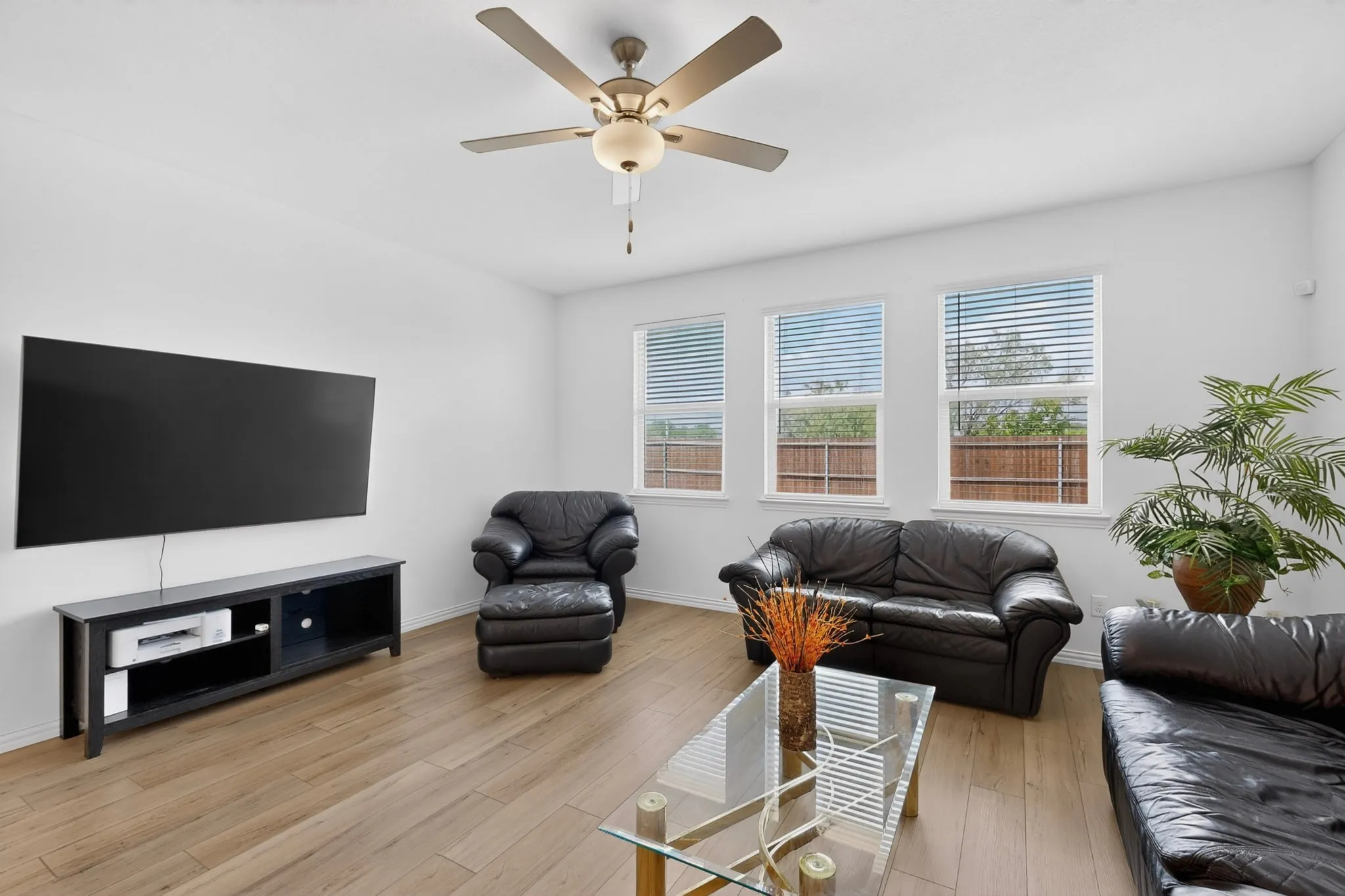 Living area featuring wood-finish flooring, white walls, and a ceiling fan with integrated lighting