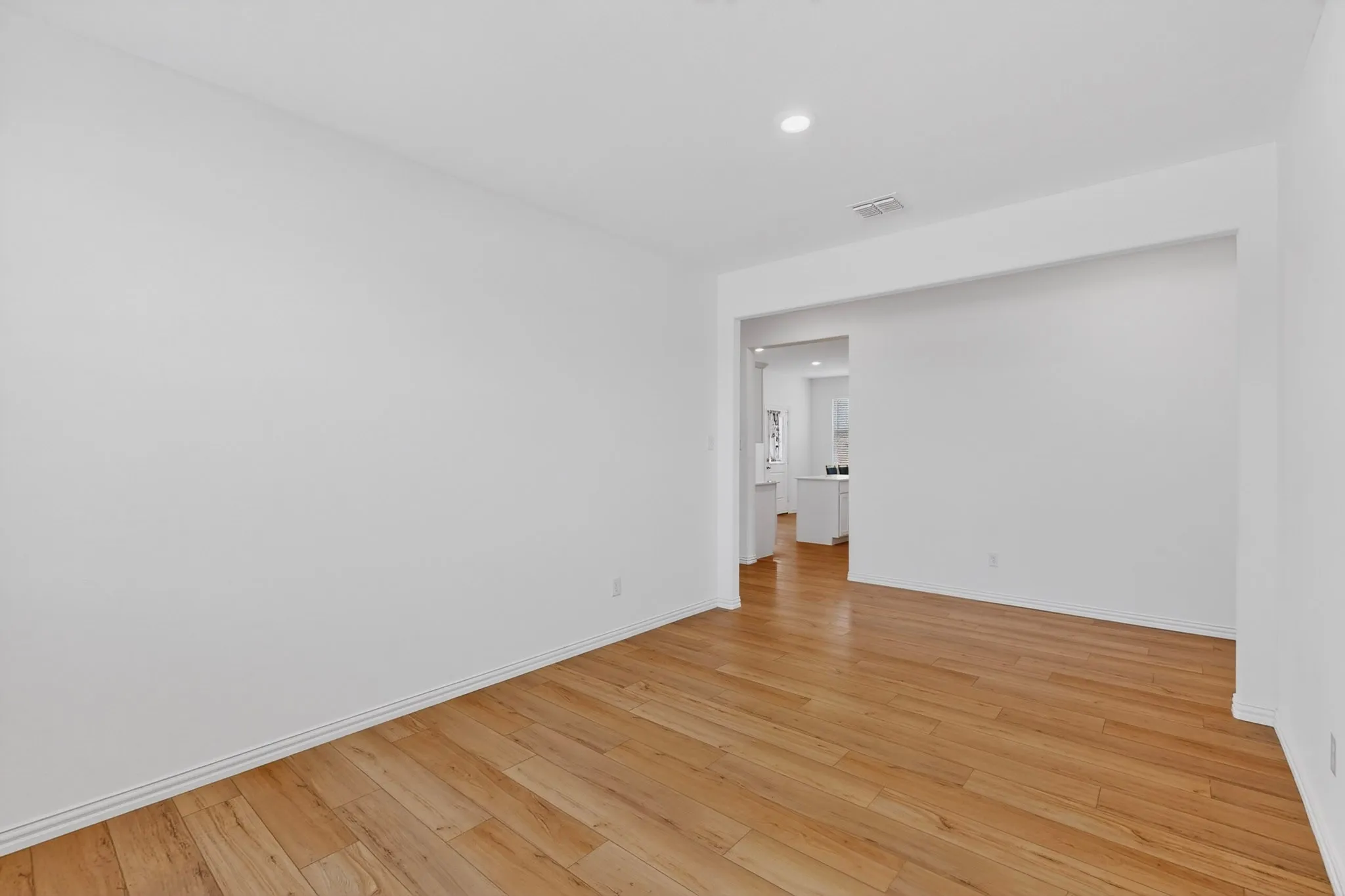 Spacious interior with wood-finish flooring, white baseboards, recessed lighting, and a broad arched entryway
