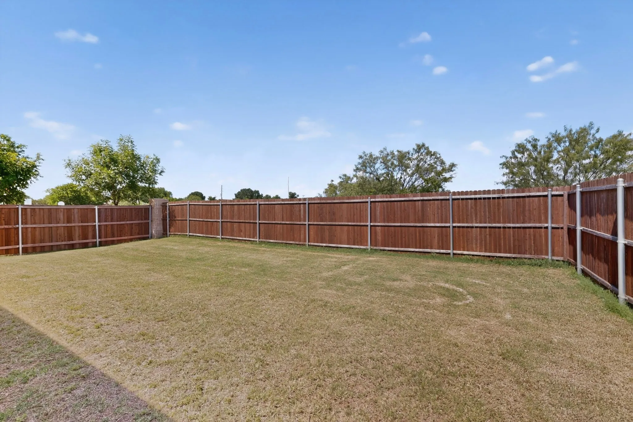 Spacious backyard with a wood privacy fence featuring metal posts, an expansive grass lawn, and mature trees beyond the property line