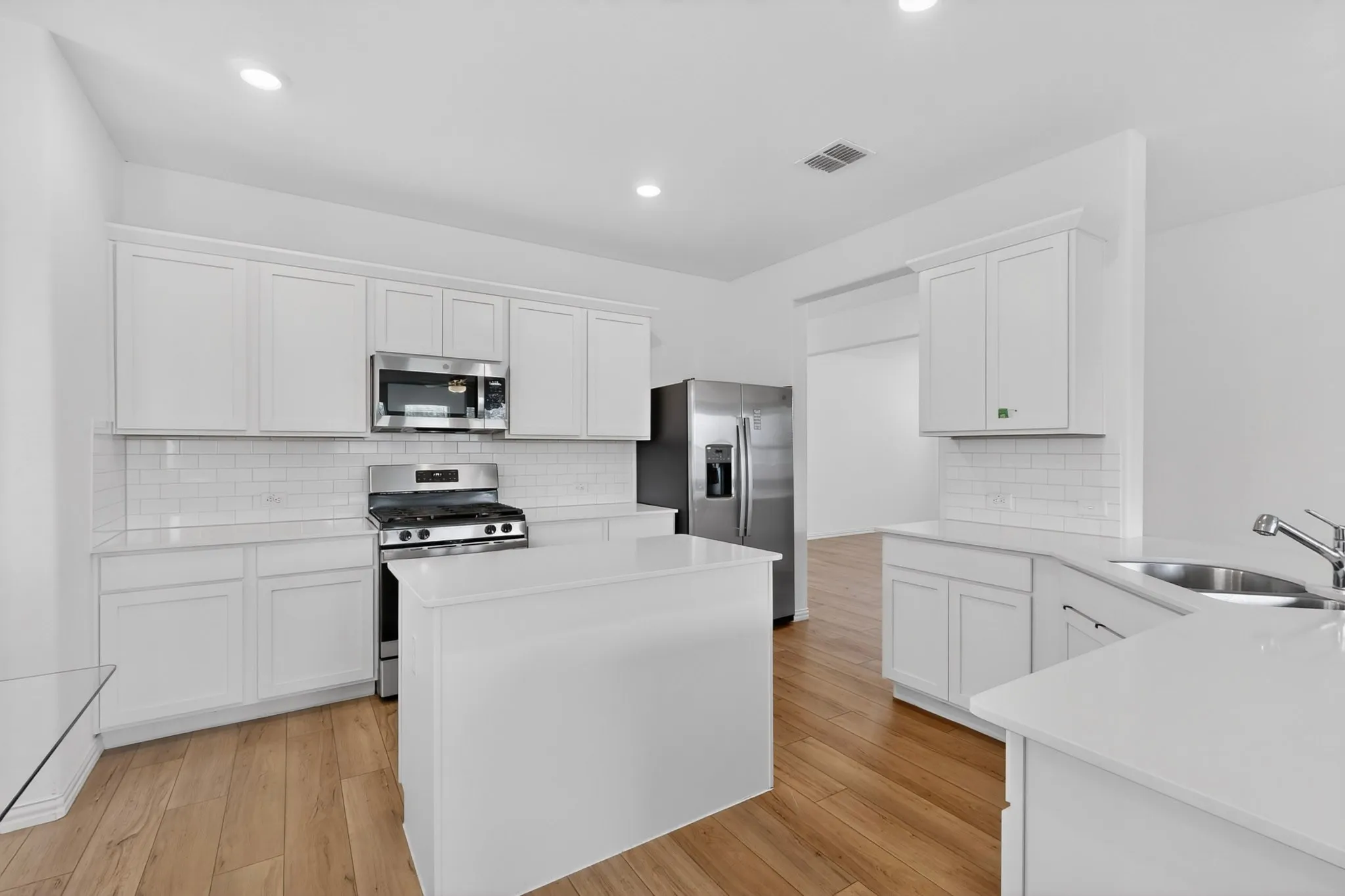 Modern kitchen featuring white shaker cabinetry, stainless steel appliances, durable wood-finish flooring, white subway tile backsplash, and recessed lighting