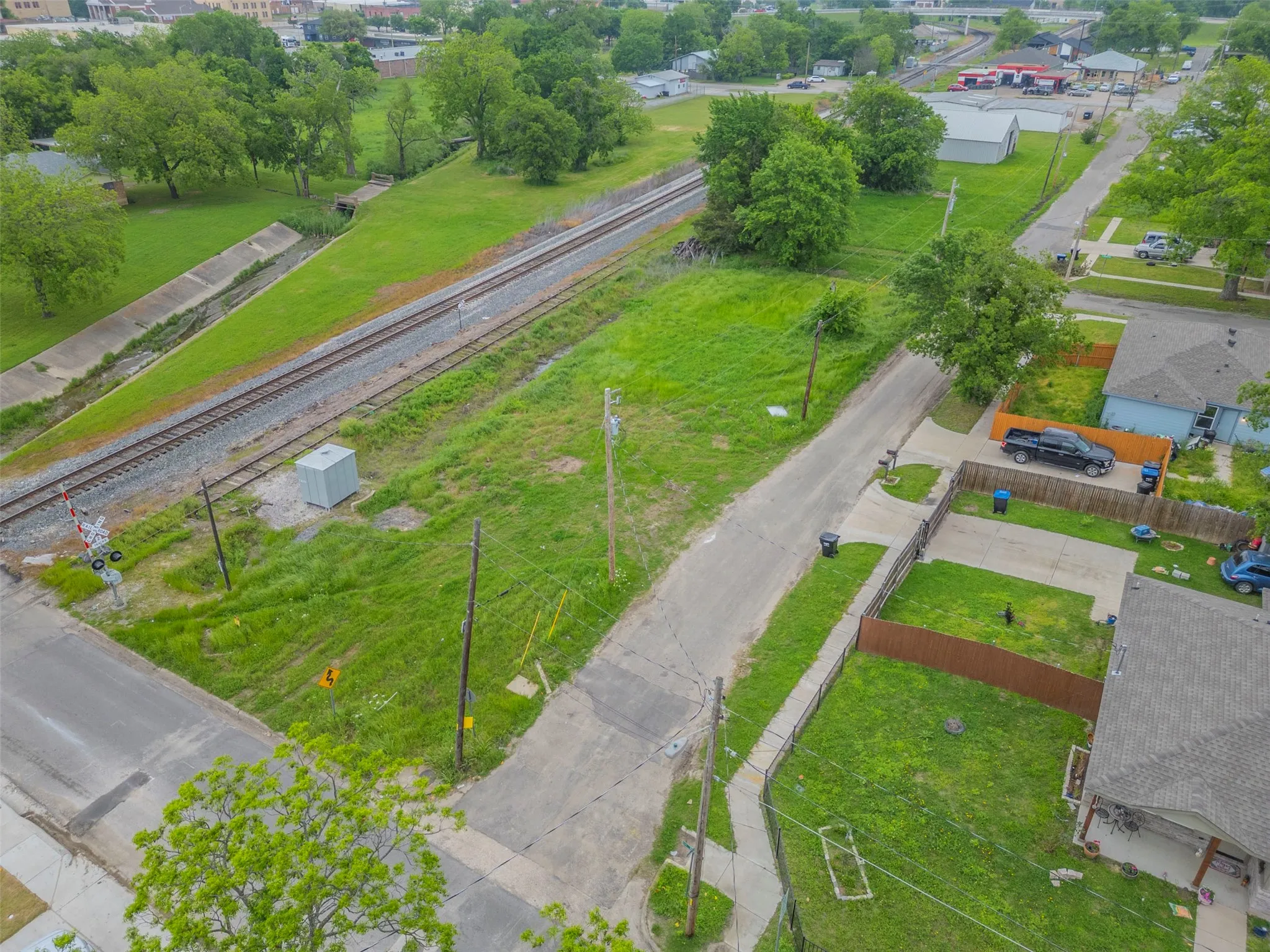 Expansive green space featuring a concrete drainage channel, railroad tracks, and mature trees