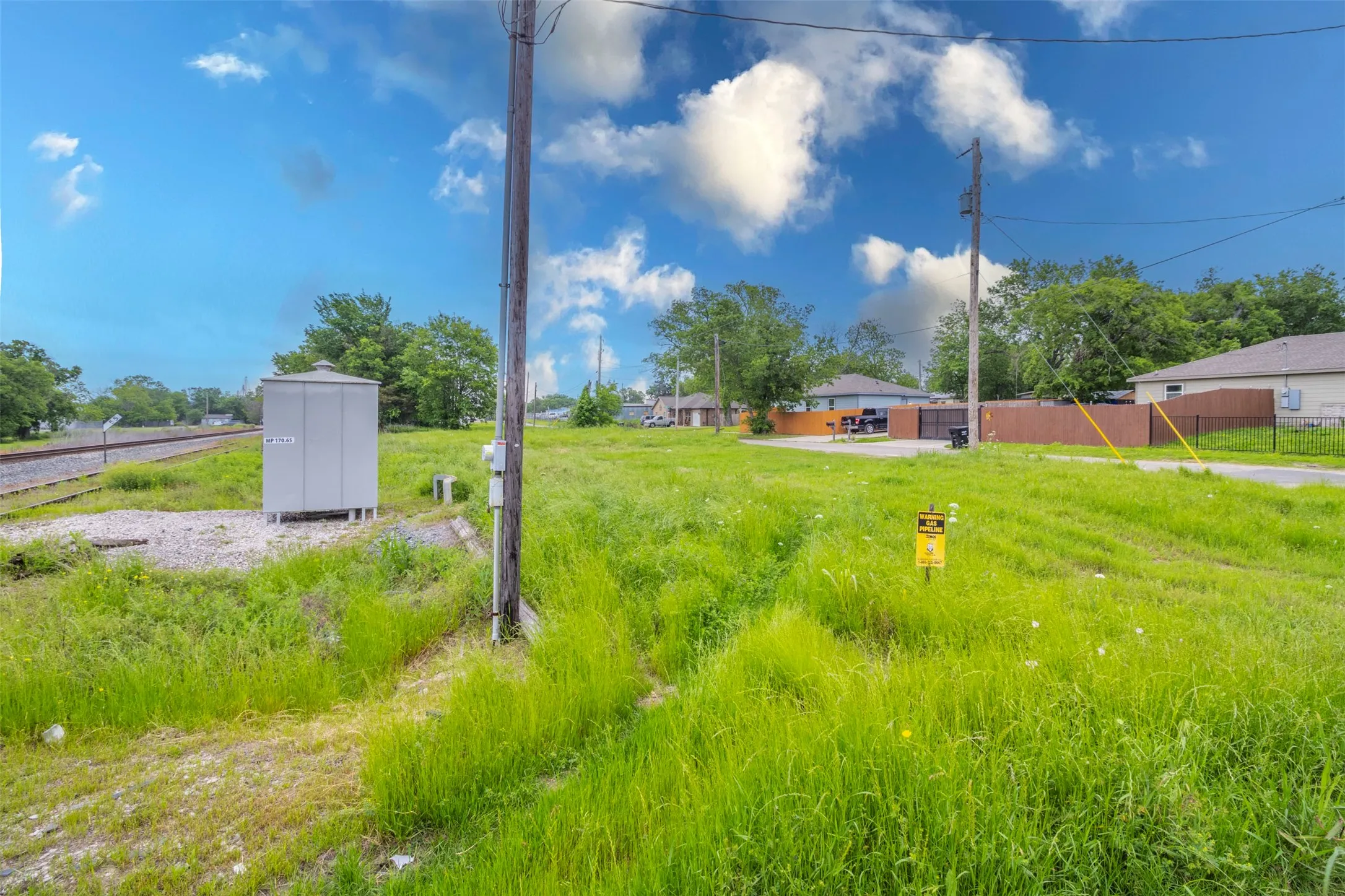 Expansive grassy lot with utility infrastructure, including a power pole and a grey utility box on a gravel base