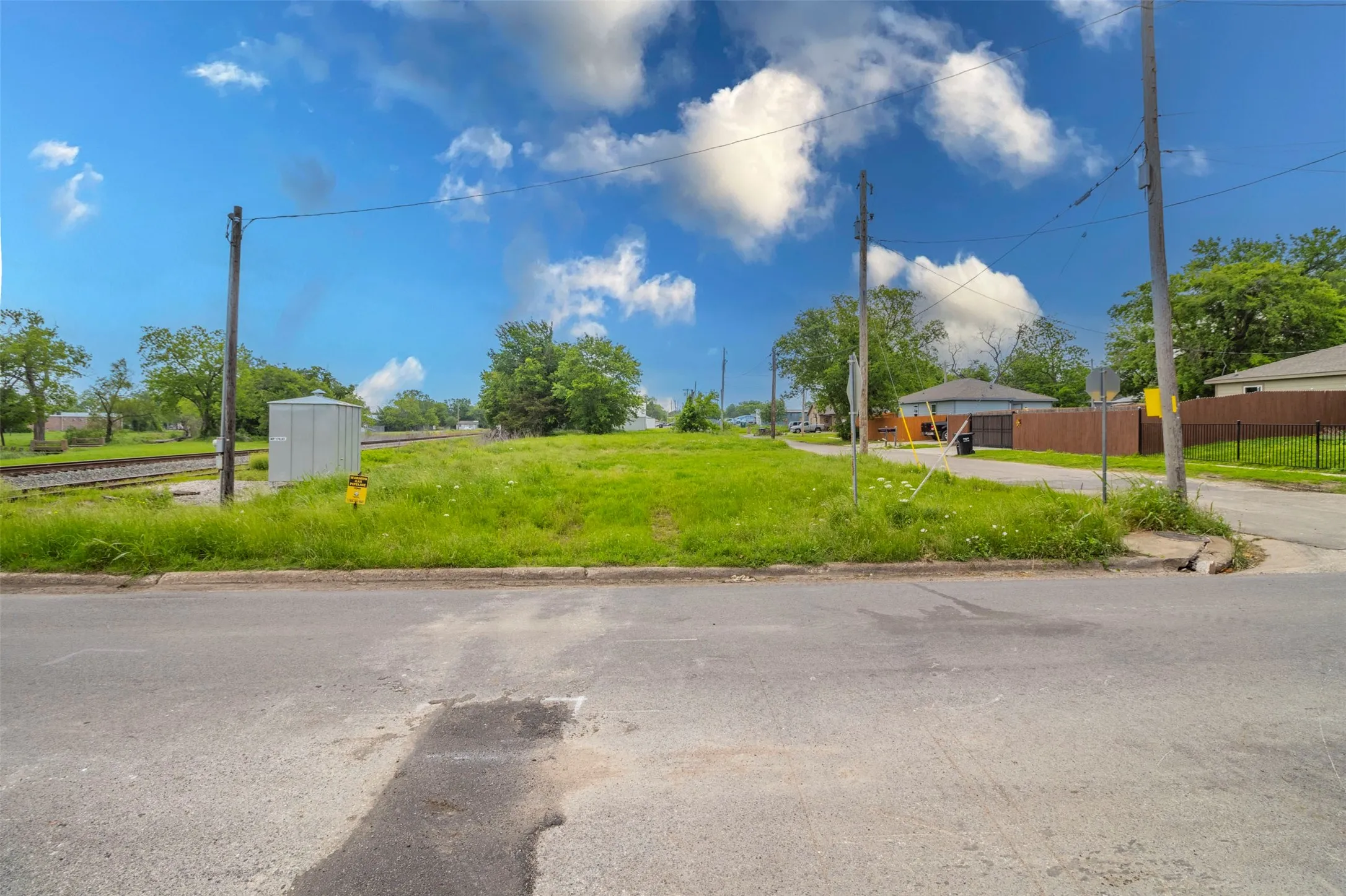 Expansive lot featuring a wide street frontage, established curb, existing utility poles, and green space