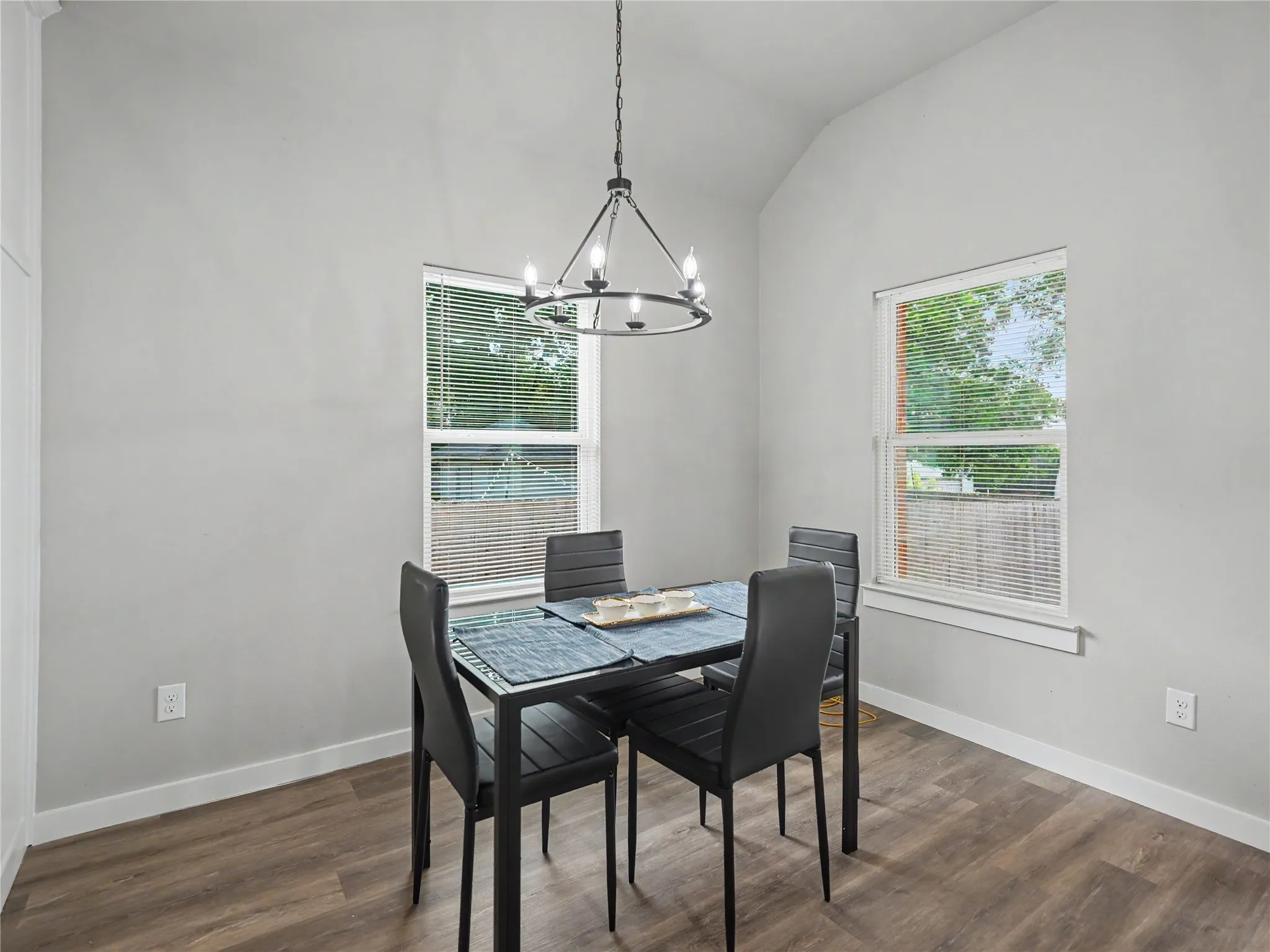 Dining area featuring wood-finish flooring, two windows with blinds, a vaulted ceiling, and a modern chandelier
