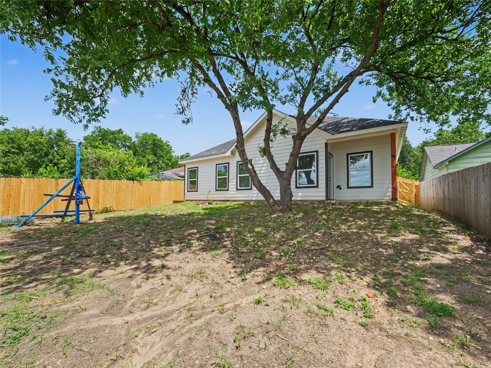 Expansive backyard featuring a mature shade tree, a newly installed wood privacy fence, and a white siding exterior with contrasting dark window frames
