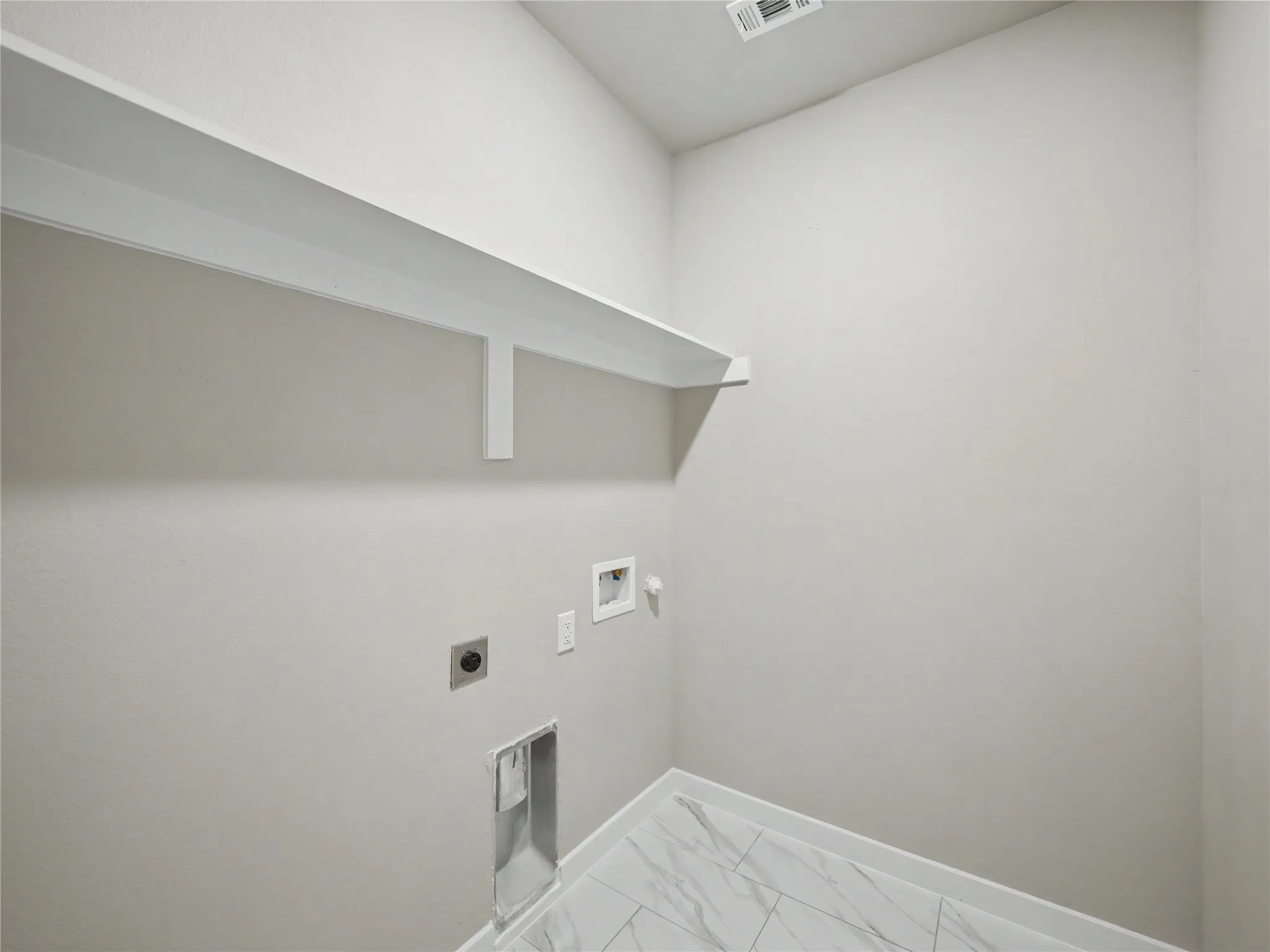 Utility room featuring a white wall shelf, textured white walls, and white baseboards