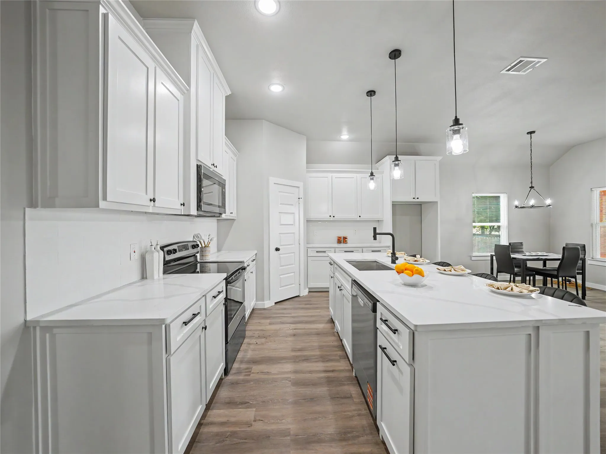 Open-concept kitchen featuring white shaker cabinetry, an expansive center island with seating, quartz countertops, stainless steel appliances, and wood-finish flooring