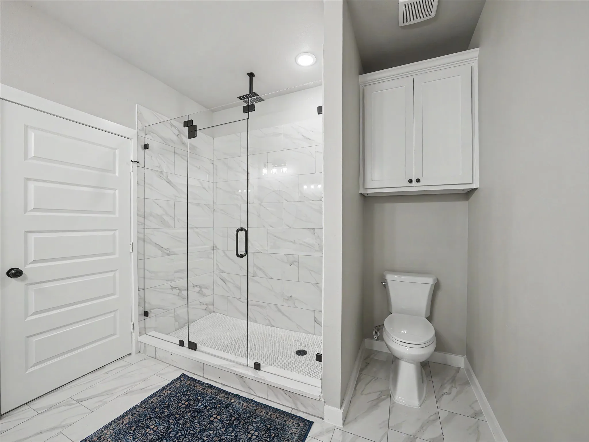 Spacious shower with glass enclosure and black hardware, complemented by large format tile flooring and shower surround