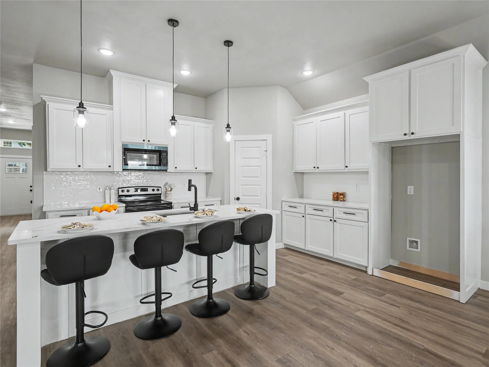 Kitchen featuring white shaker cabinetry, an island with countertop seating, wood-finish flooring, a white tile backsplash, and recessed lighting