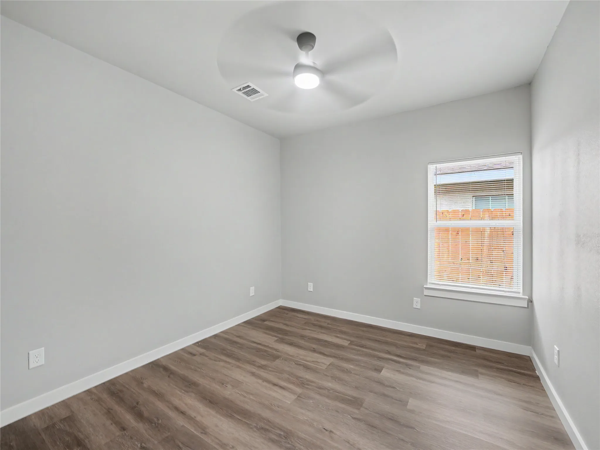 Room featuring wood-finish flooring, light gray walls, white trim, and a ceiling fan with integrated lighting