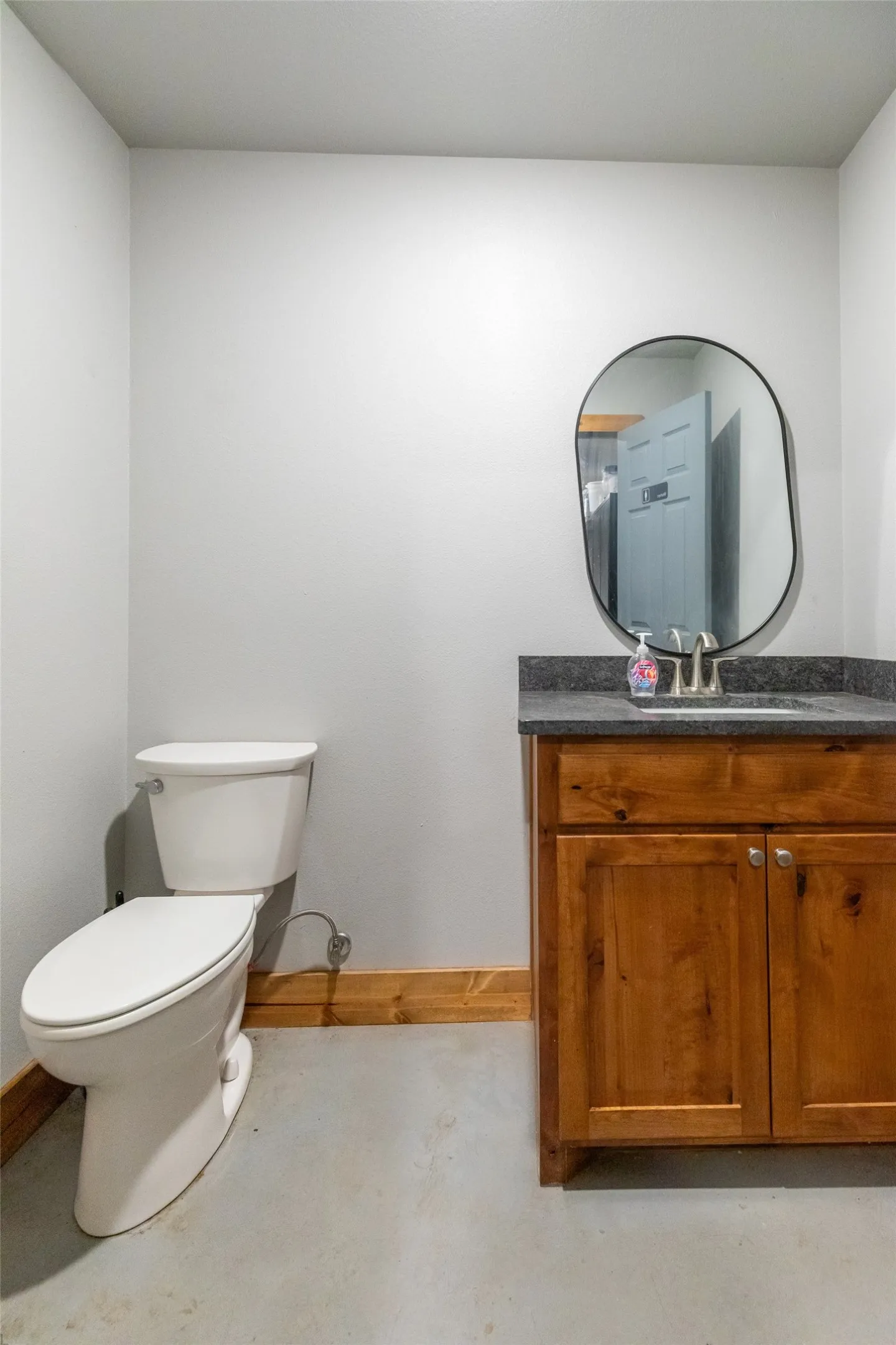 Bathroom featuring a wood-finish vanity with a dark countertop and undermount sink, illuminated by an organic-shaped mirror