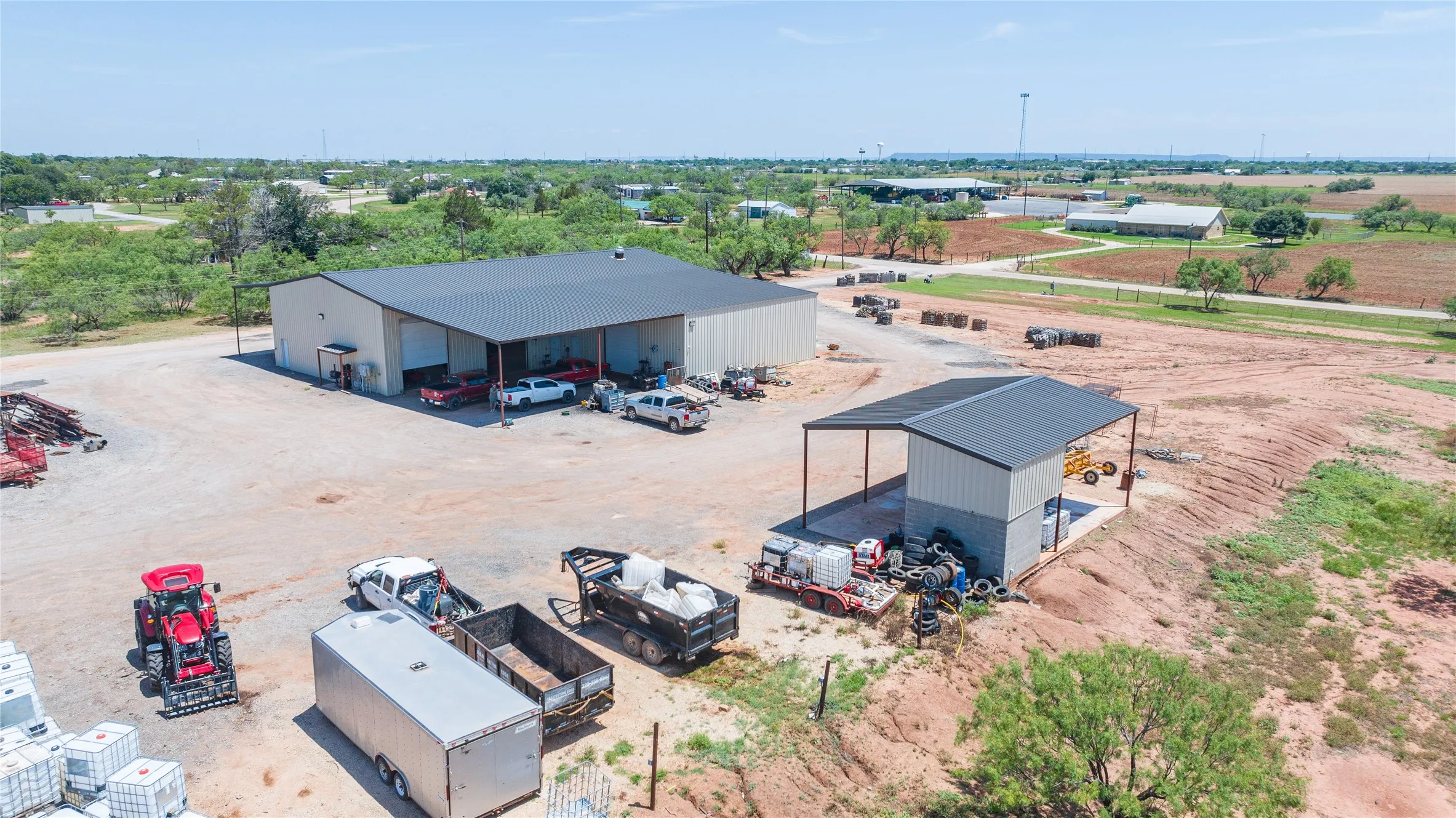 Expansive open-air property featuring a large metal building with multiple bay doors and an attached covered​​‌​​​​‌​​‌‌​‌‌​​​‌‌​‌​‌​‌​​​‌​​ area