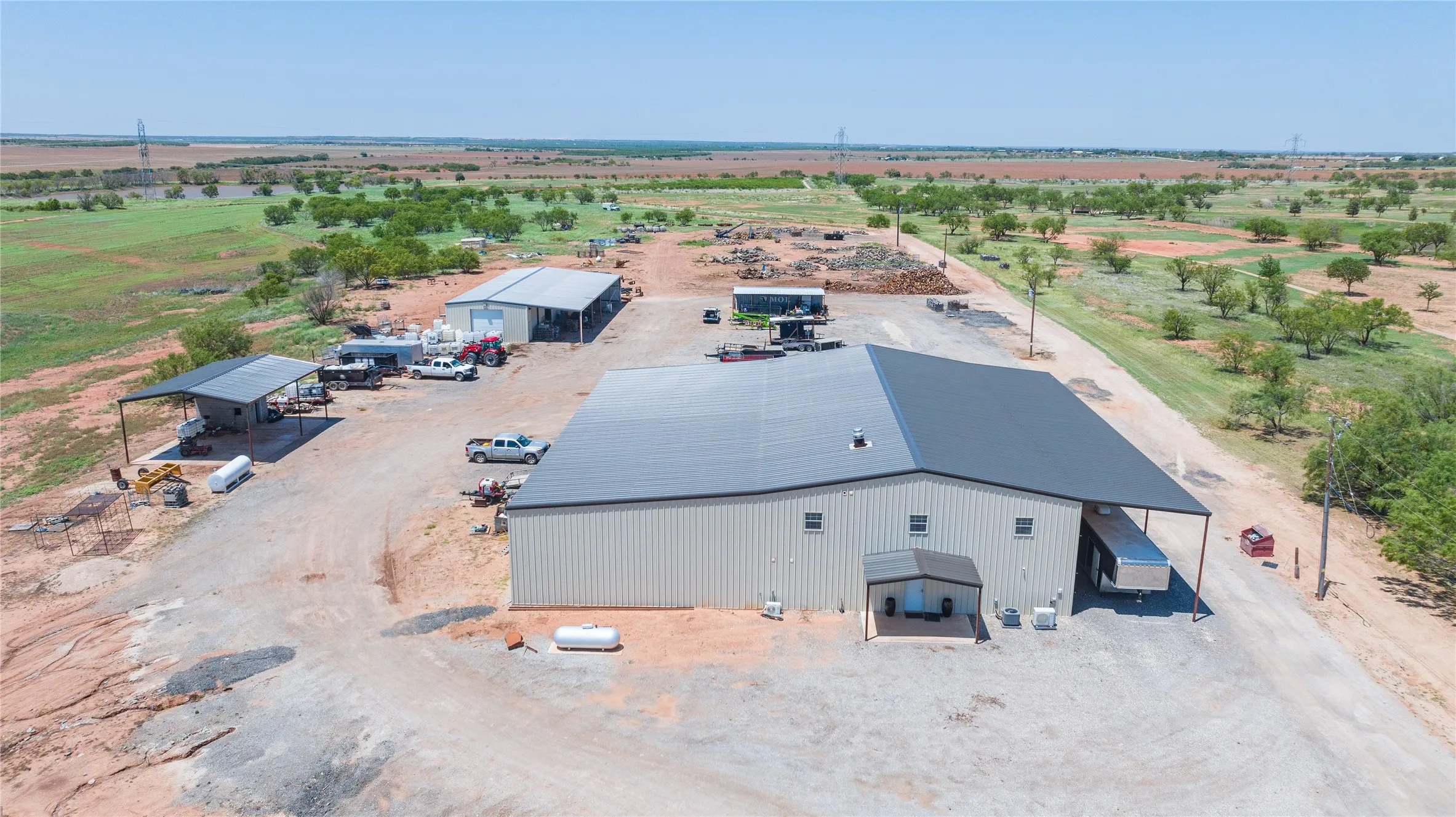 Industrial property featuring two metal buildings with dark metal roofs, a covered carport, and extensive gravel surfacing