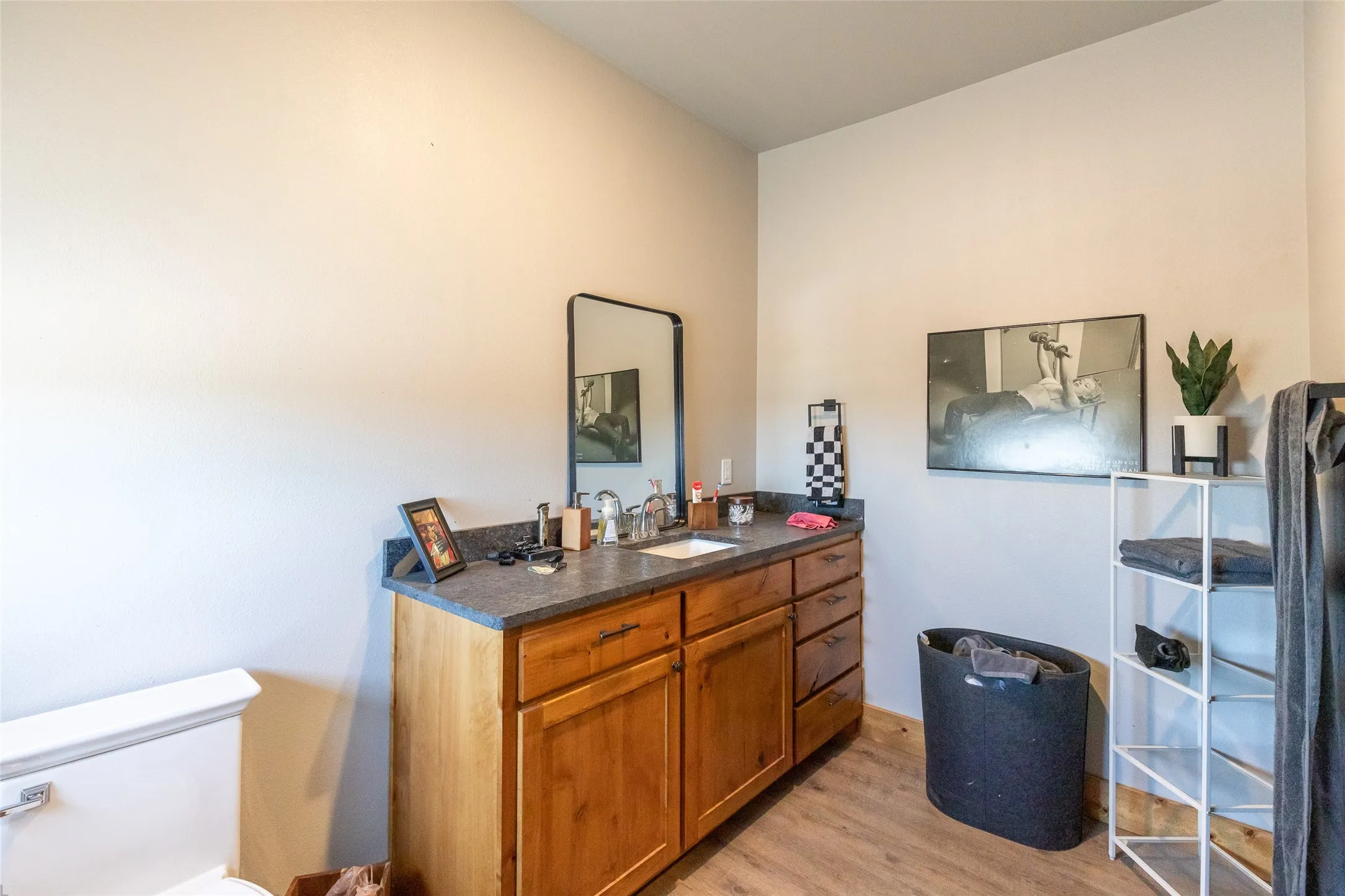 Single vanity featuring wood-finish cabinetry, a dark countertop, and an undermount sink