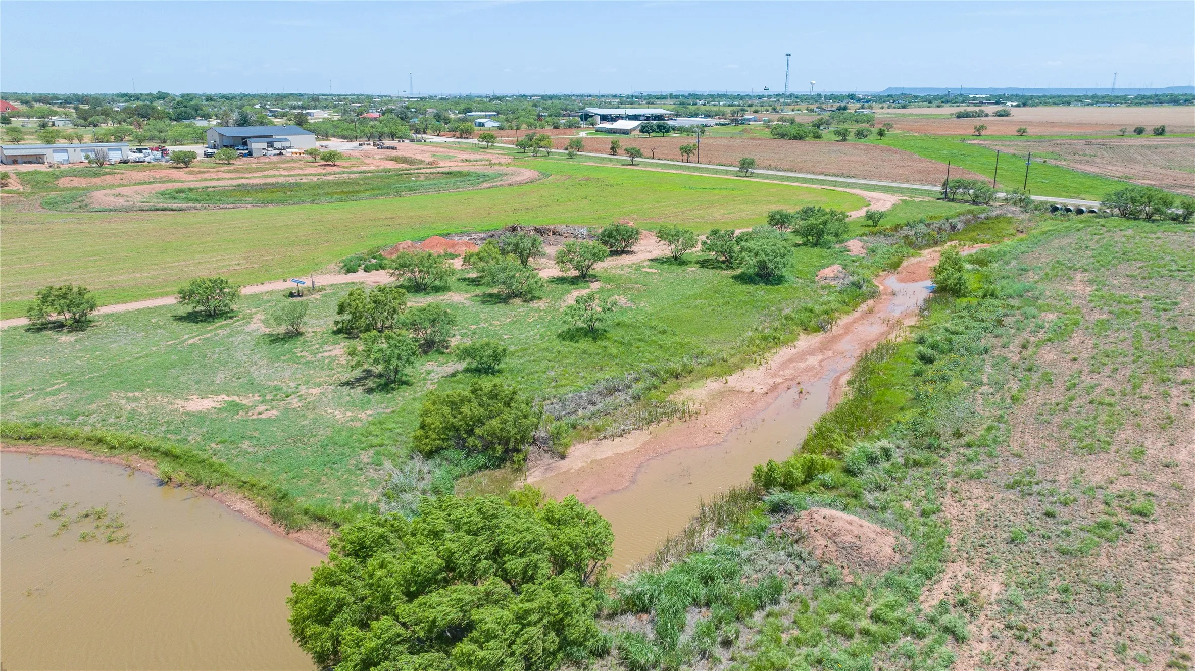 Expansive land offering a tranquil pond, natural water feature, scattered mature trees, and a distant bridge structure