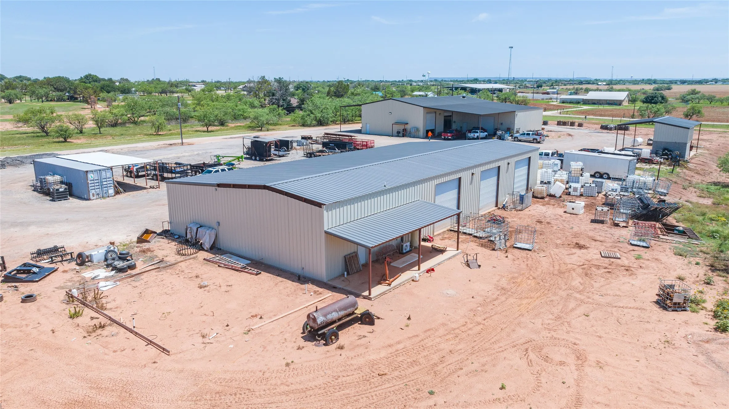 Expansive commercial property featuring multiple metal buildings with roll-up doors, a covered entry, and substantial outdoor storage space
