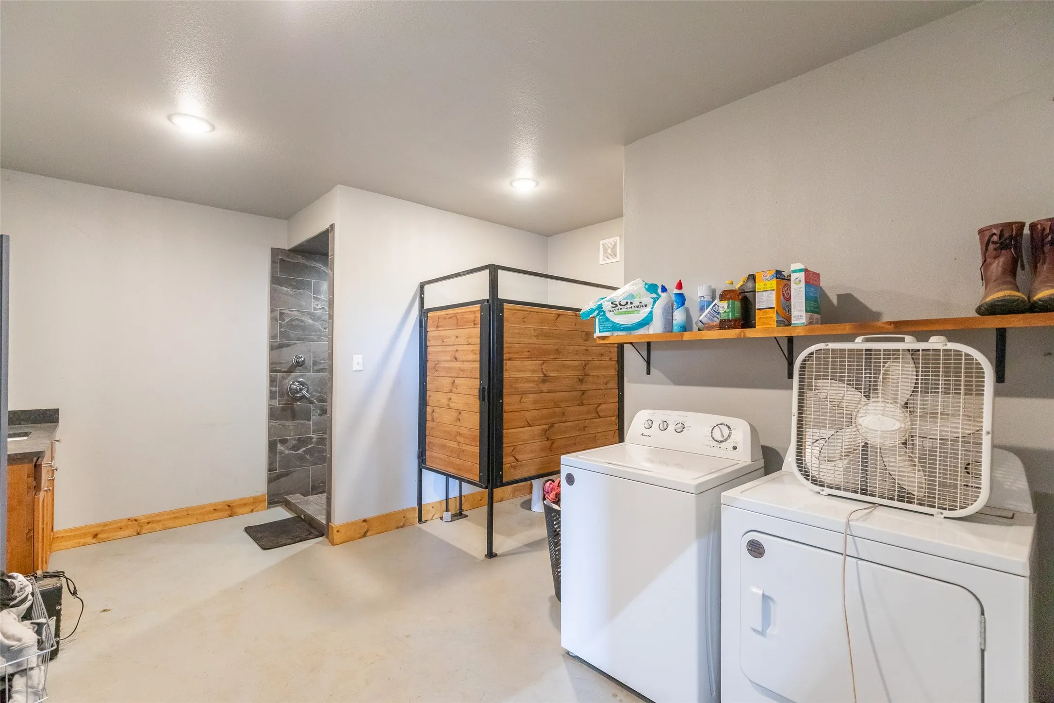 Utility space featuring a walk-in shower with dark gray tile, light gray walls, and wood-finish trim