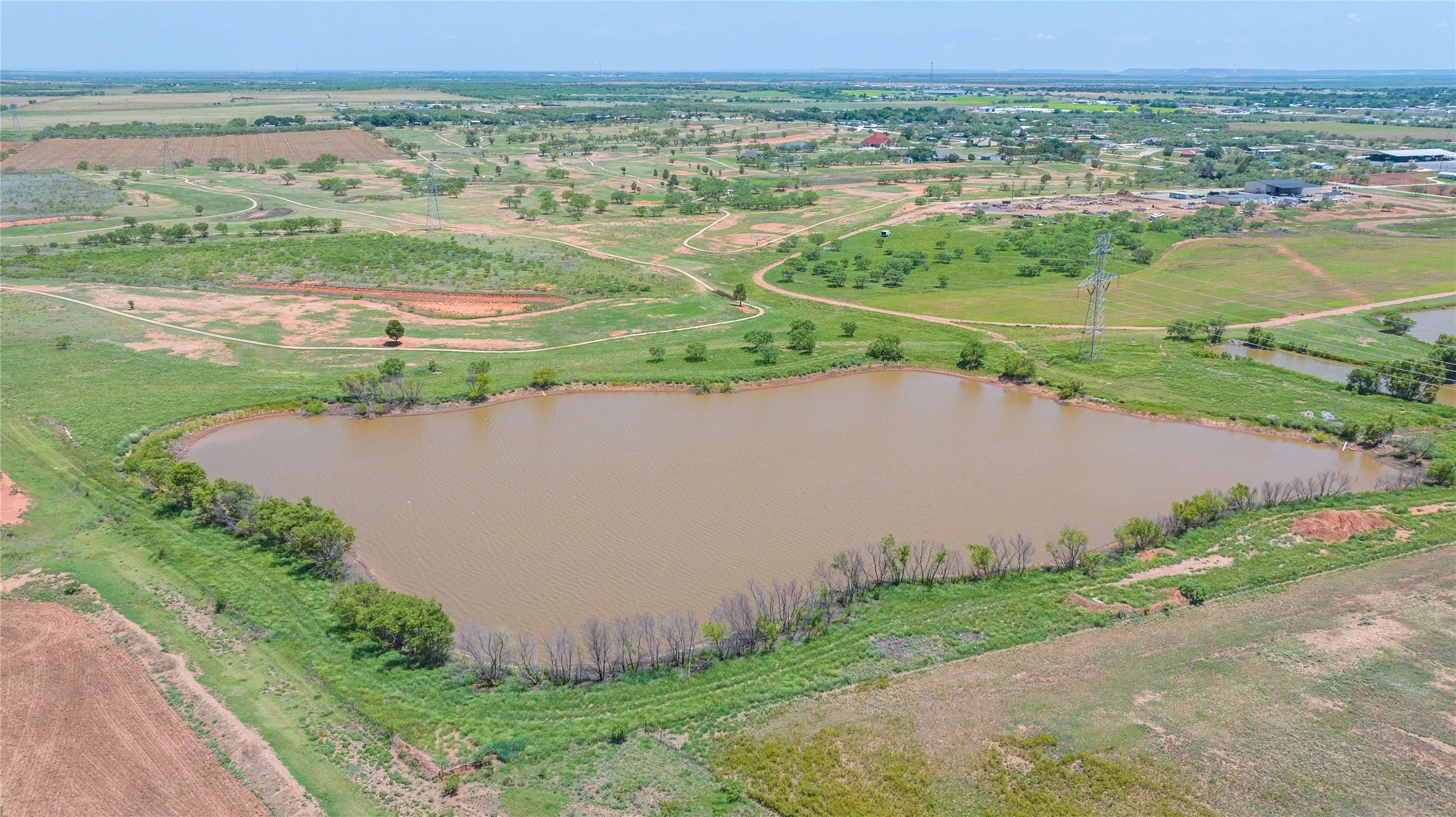 Expansive land parcel featuring a large pond, surrounded by green fields and scattered trees