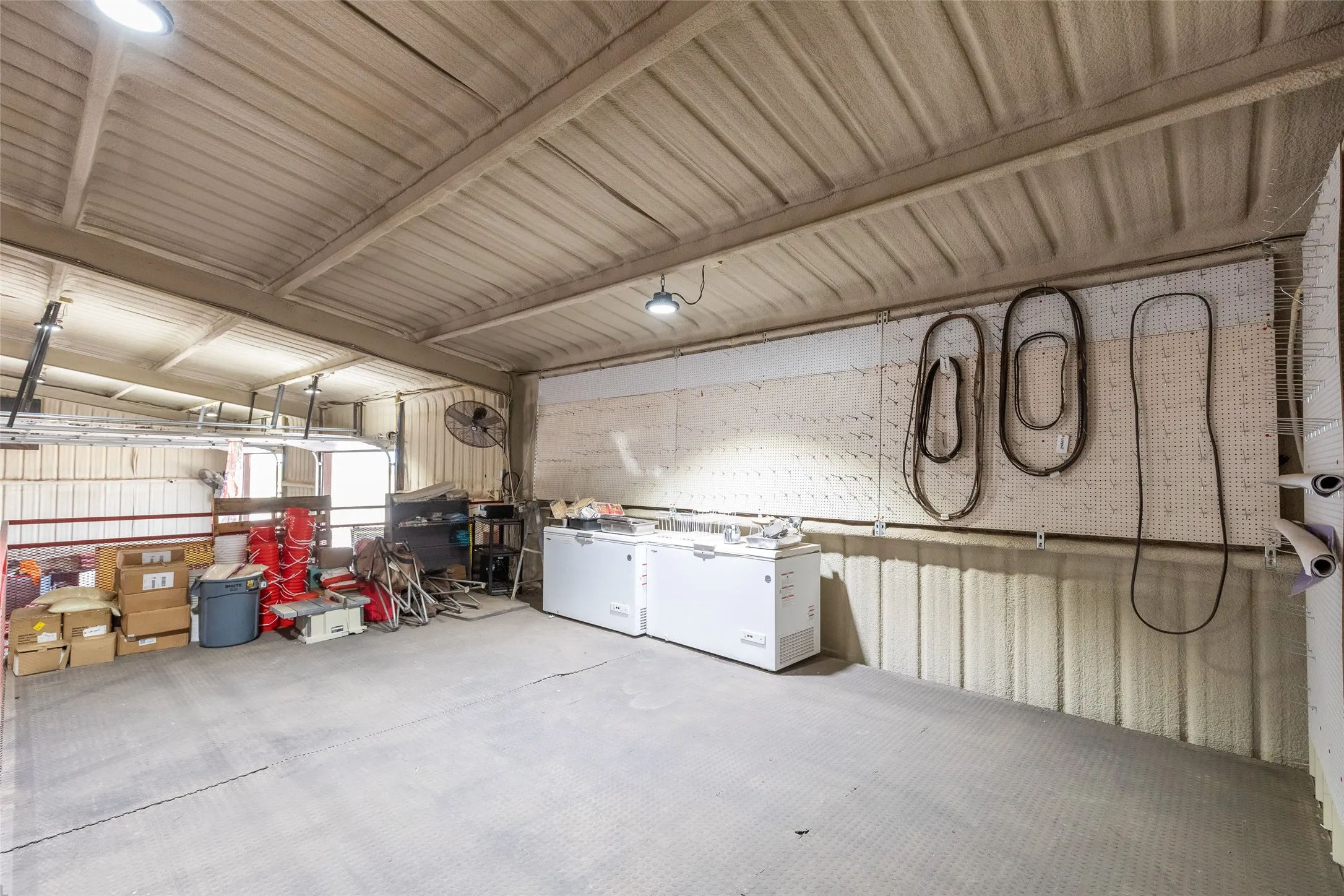 Spacious garage or workshop featuring a textured ceiling, durable flooring, integrated lighting, and a pegboard storage system