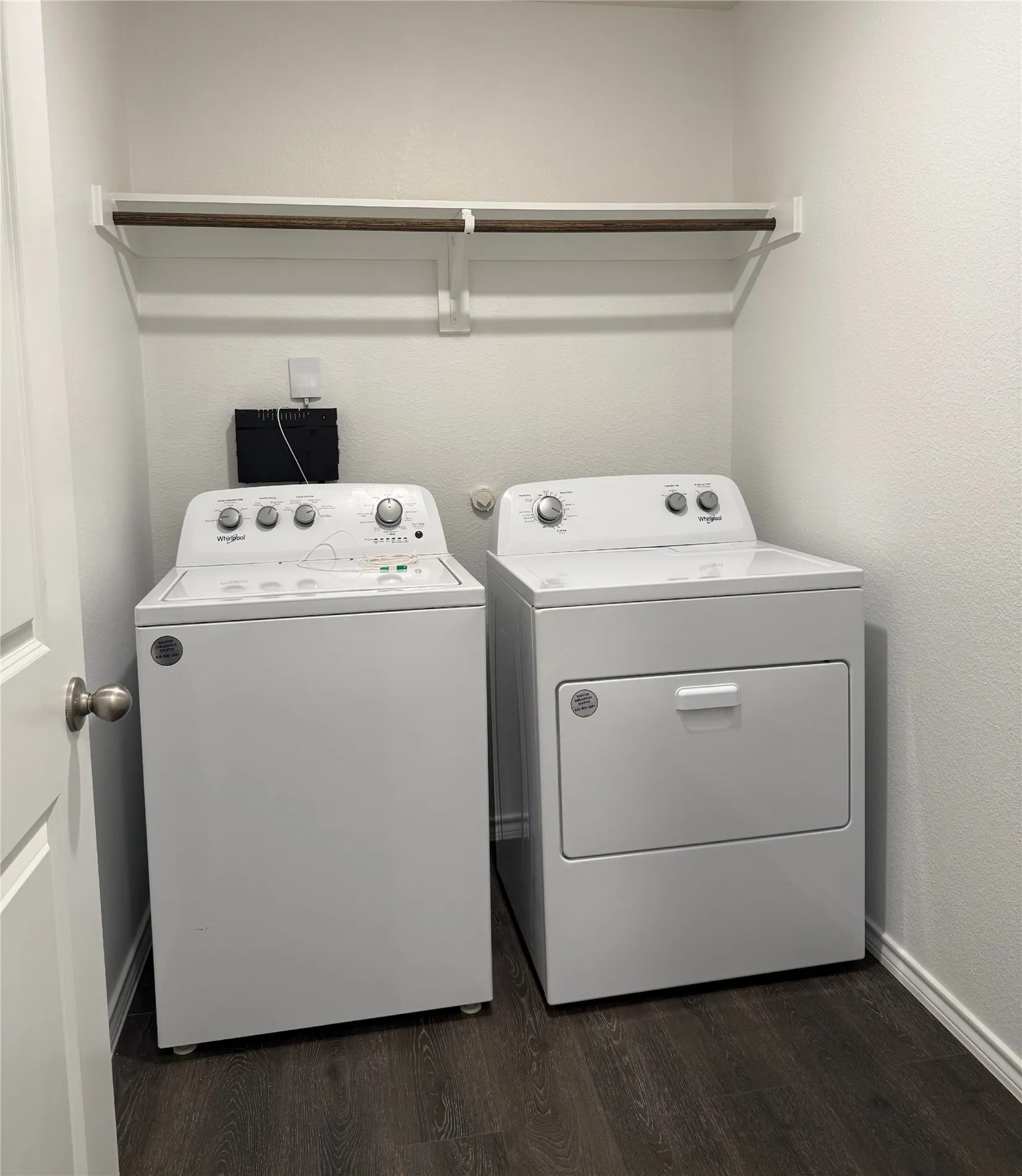 Dedicated laundry area featuring wood-finish flooring, a wall-mounted shelving unit with a hanging rod, and light-toned wall finishes