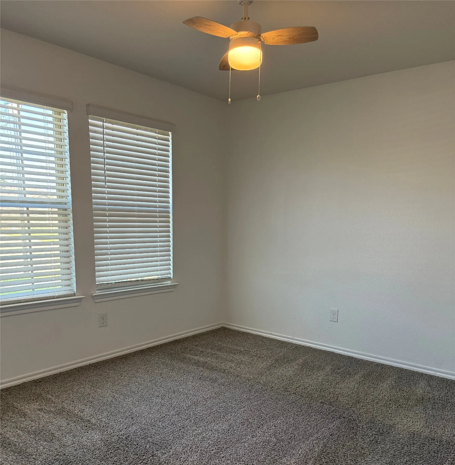 Interior space featuring dual windows with blinds, overhead ceiling fan with light fixture, neutral wall finishes, and soft carpeting