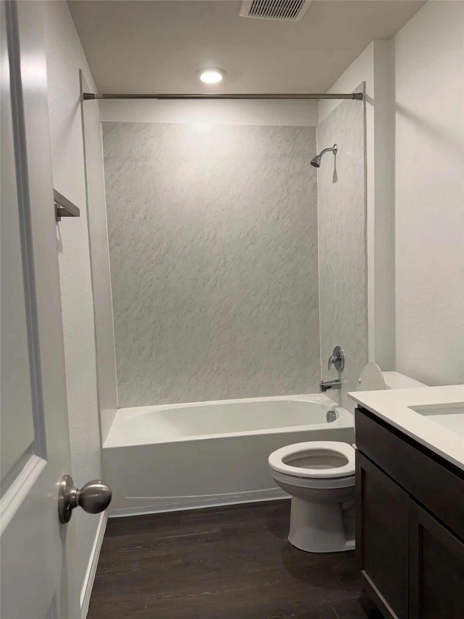 Bathroom featuring a white tub, textured shower surround, and dark wood-finish flooring