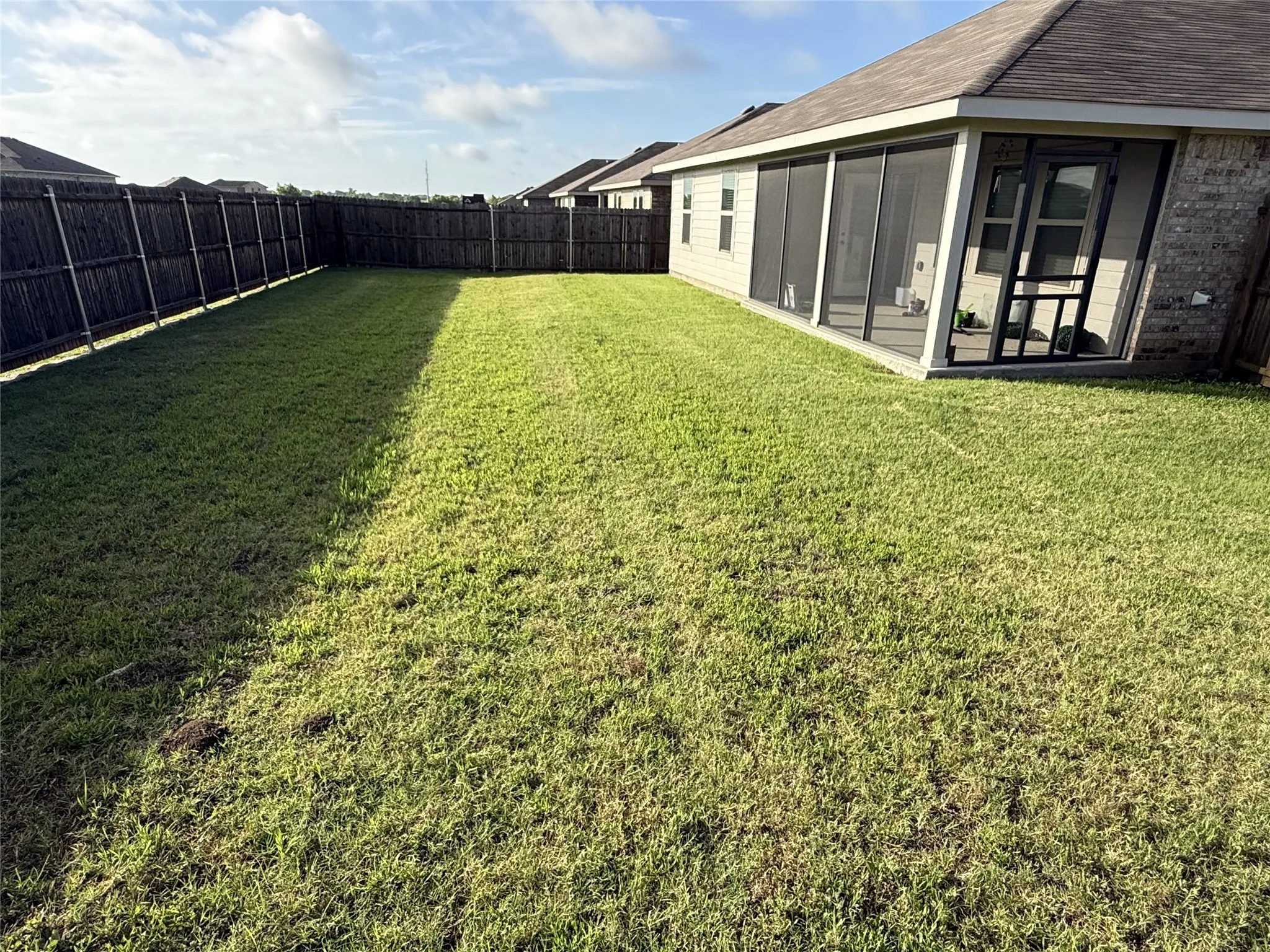 Expansive green lawn with a screened-in porch, privacy fencing, and brick exterior accents