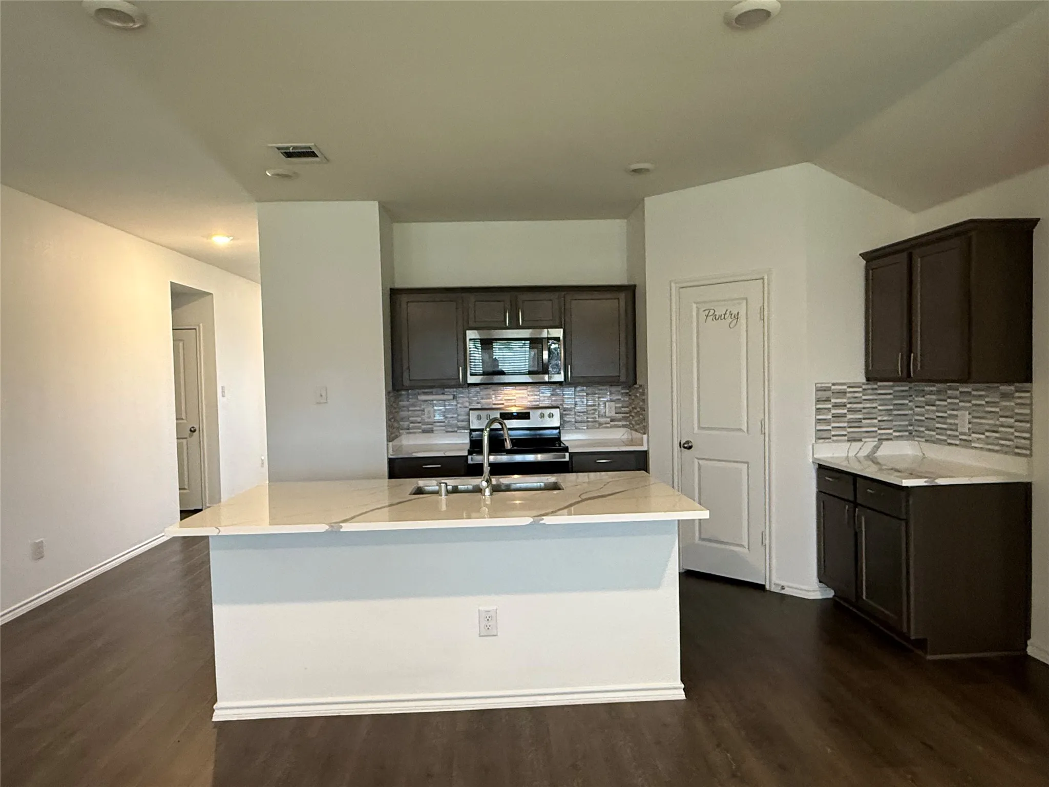 Kitchen featuring a central island with countertop seating, dark wood-finish cabinetry, stainless steel appliances, and wood-finish flooring