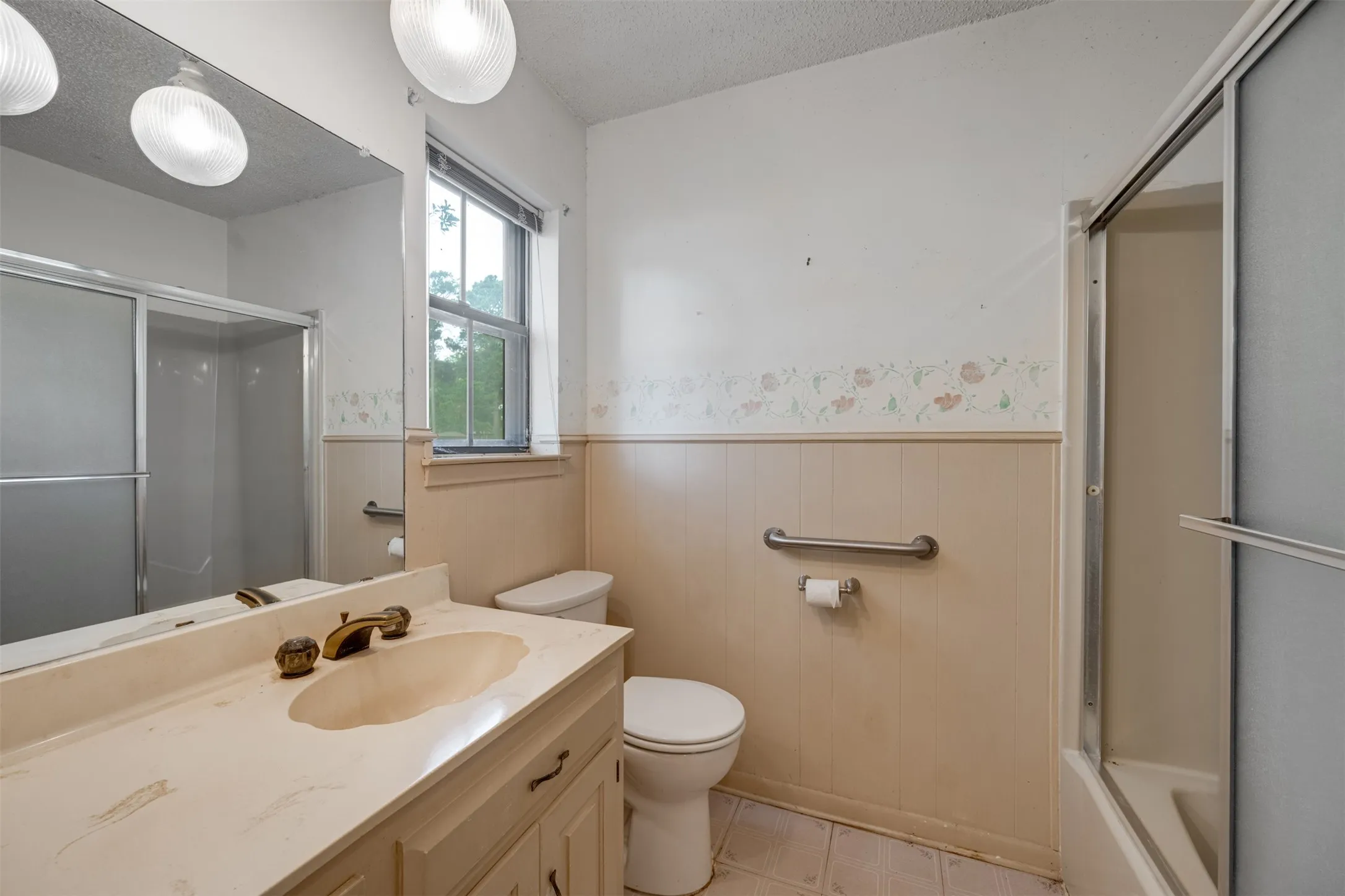 Bathroom vanity with an integrated sink, dual light fixtures, a large wall mirror, and a window providing natural light