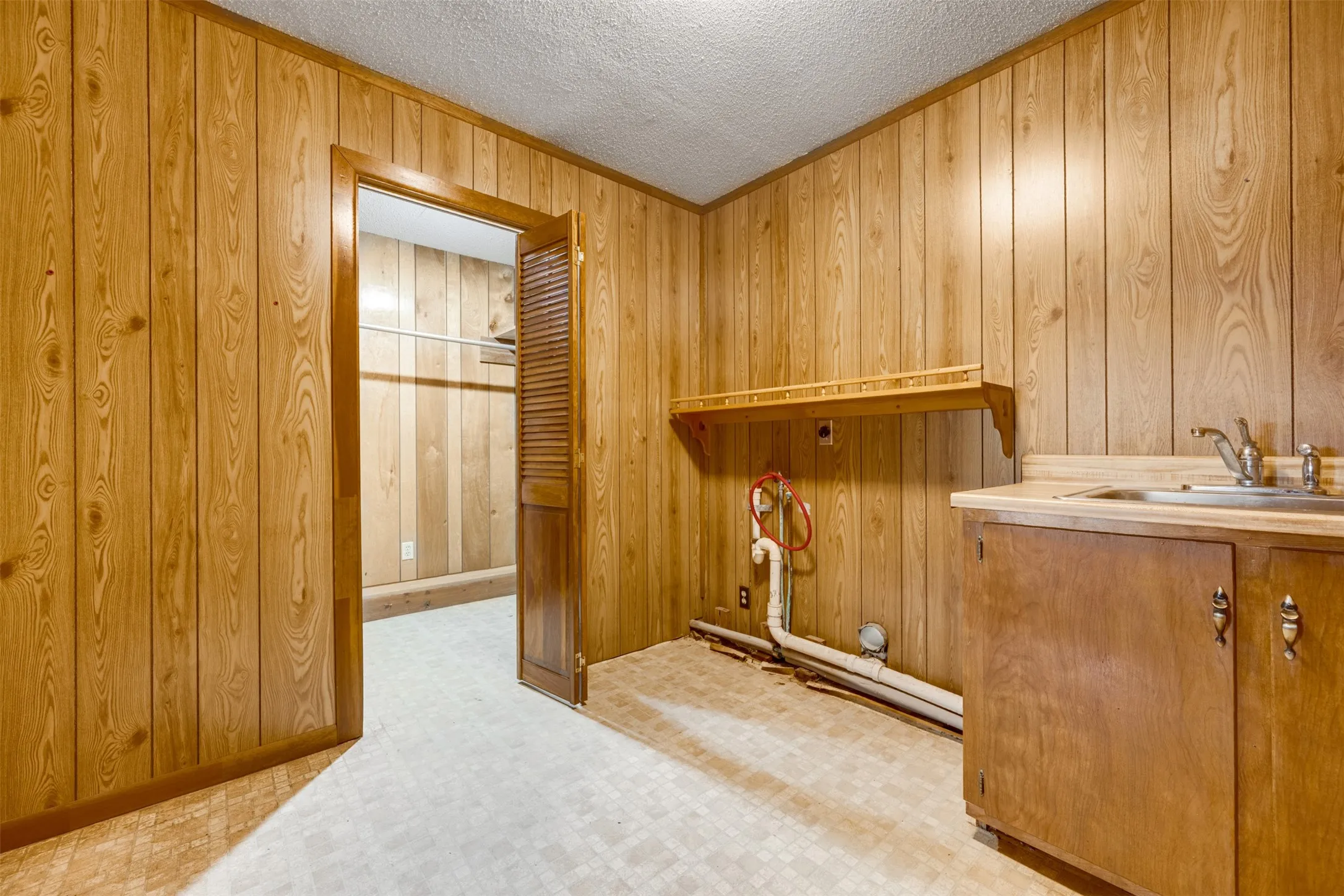 Utility room featuring wood-finish paneling, a built-in countertop with an integrated sink, base cabinetry, and a wall-mounted shelf