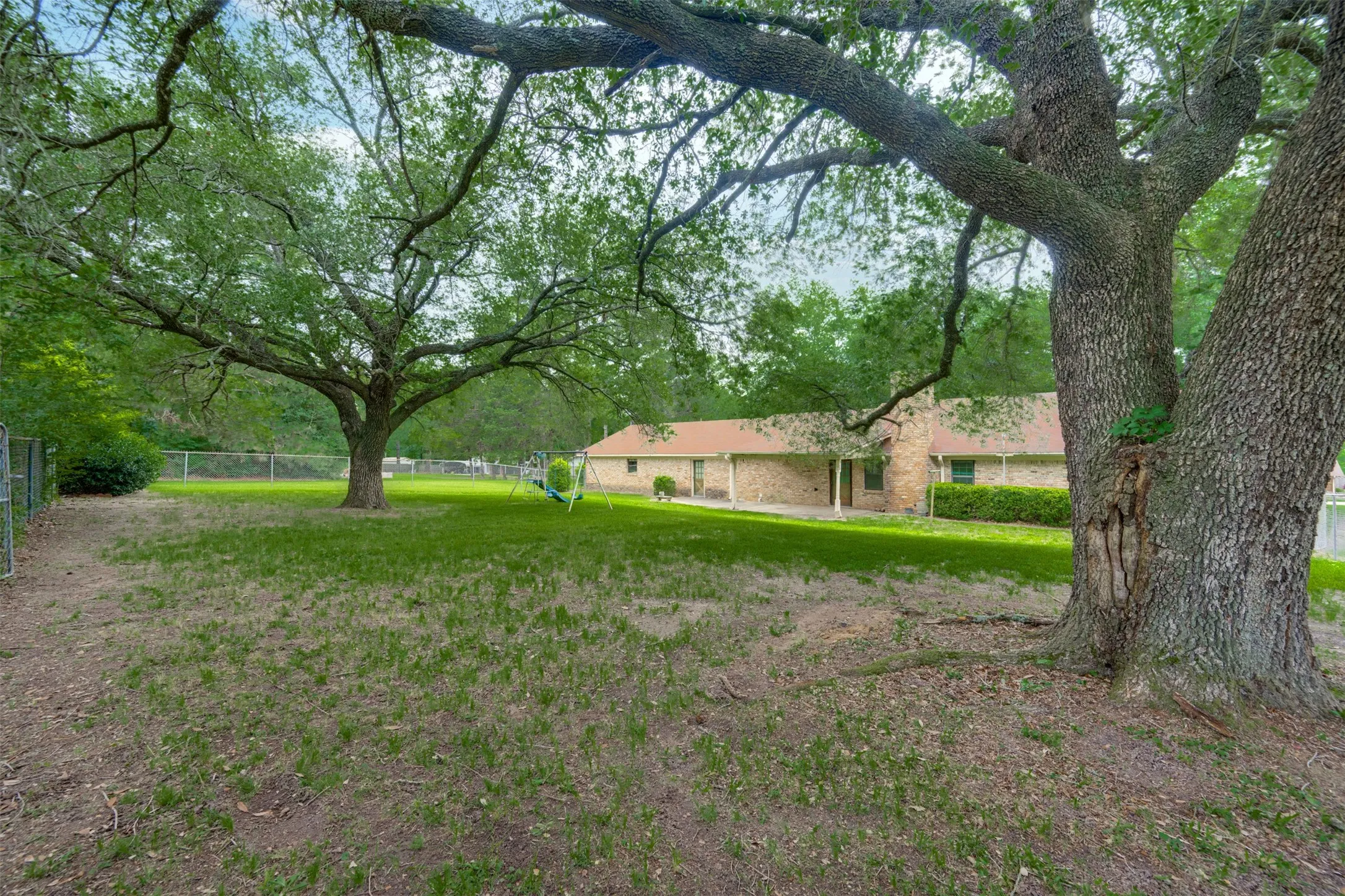 Expansive backyard featuring mature trees, a manicured lawn, and a perimeter chain-link fence