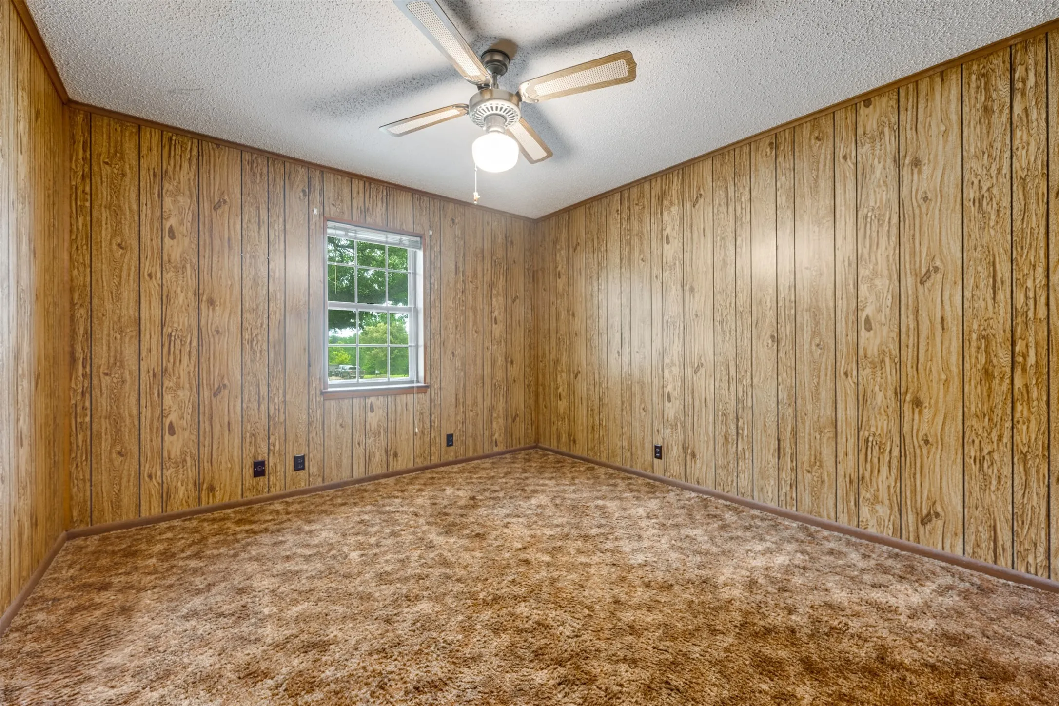 Room featuring wood-paneled walls, a single-pane window, and a ceiling fan with integrated lighting