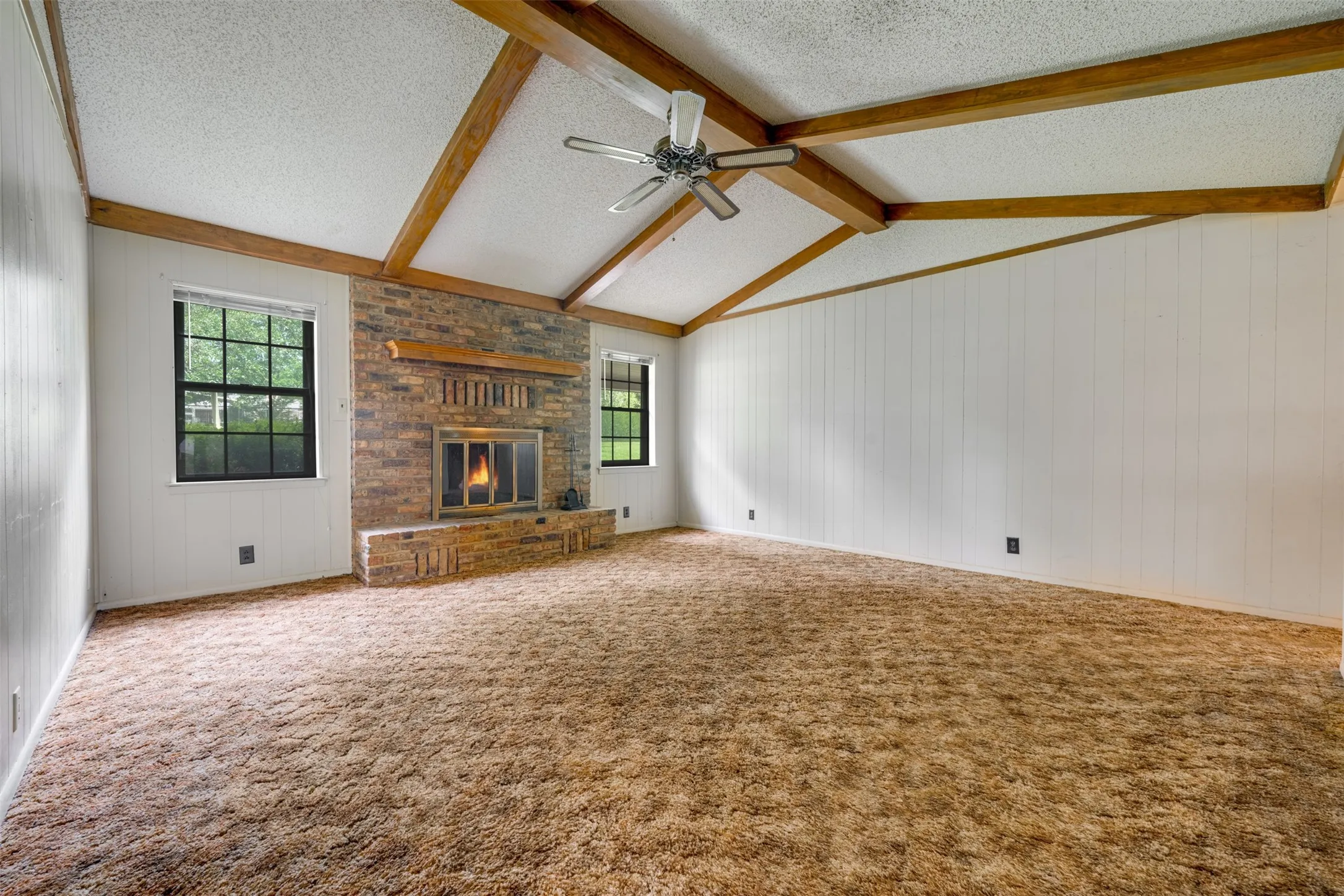 Spacious interior with vaulted ceilings, exposed wood beams, and a prominent brick fireplace with a wood mantle