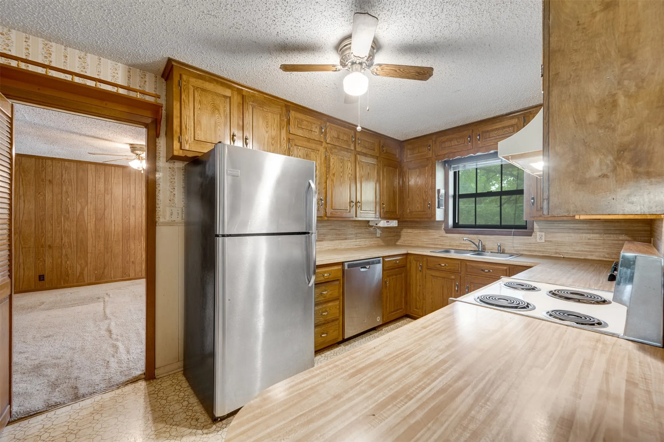 Kitchen featuring wood cabinetry, stainless steel refrigerator and dishwasher, electric range, and wood-finish countertops