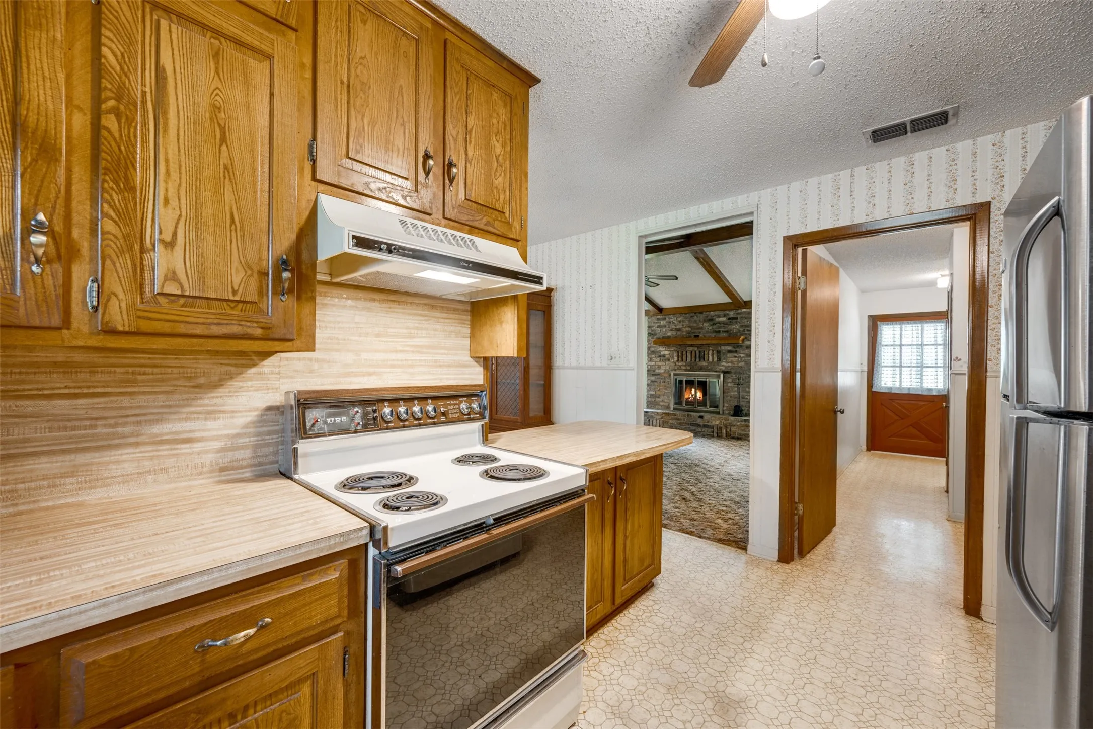 Kitchen featuring wood cabinetry, laminate countertops, and a built-in range with overhead vent hood