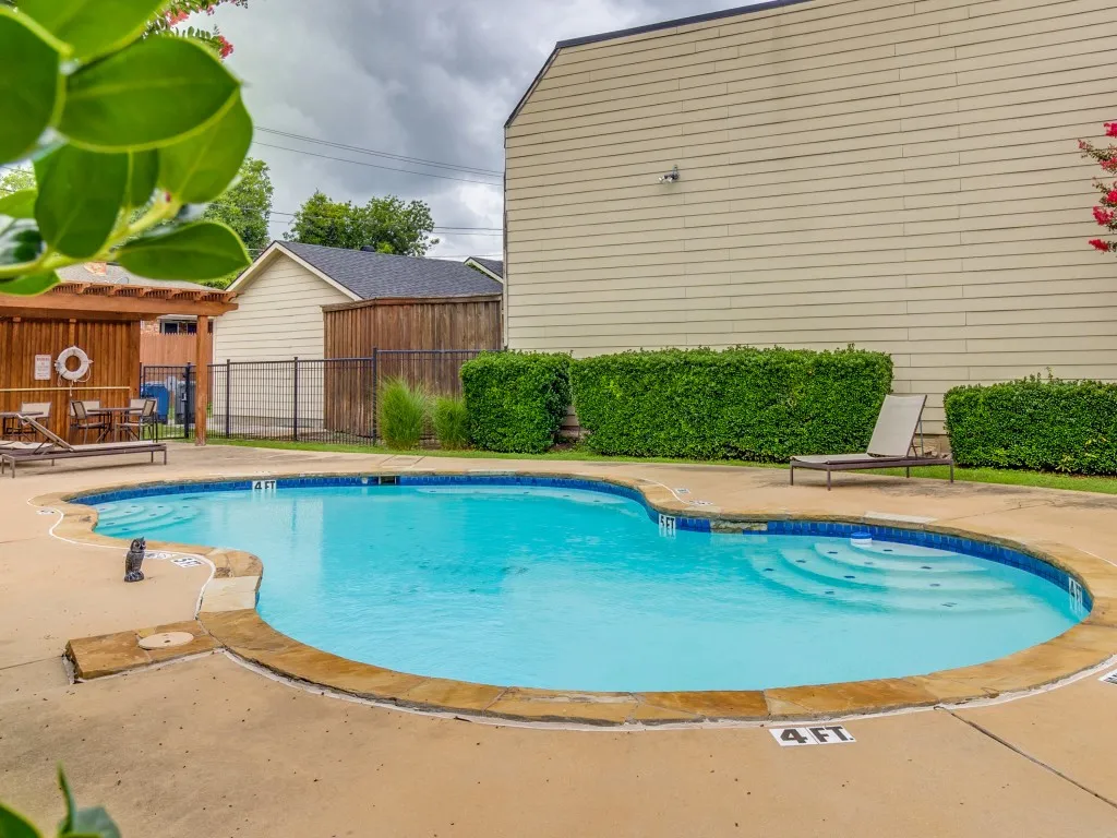 Freeform swimming pool with integrated steps, surrounded by concrete decking and natural stone coping