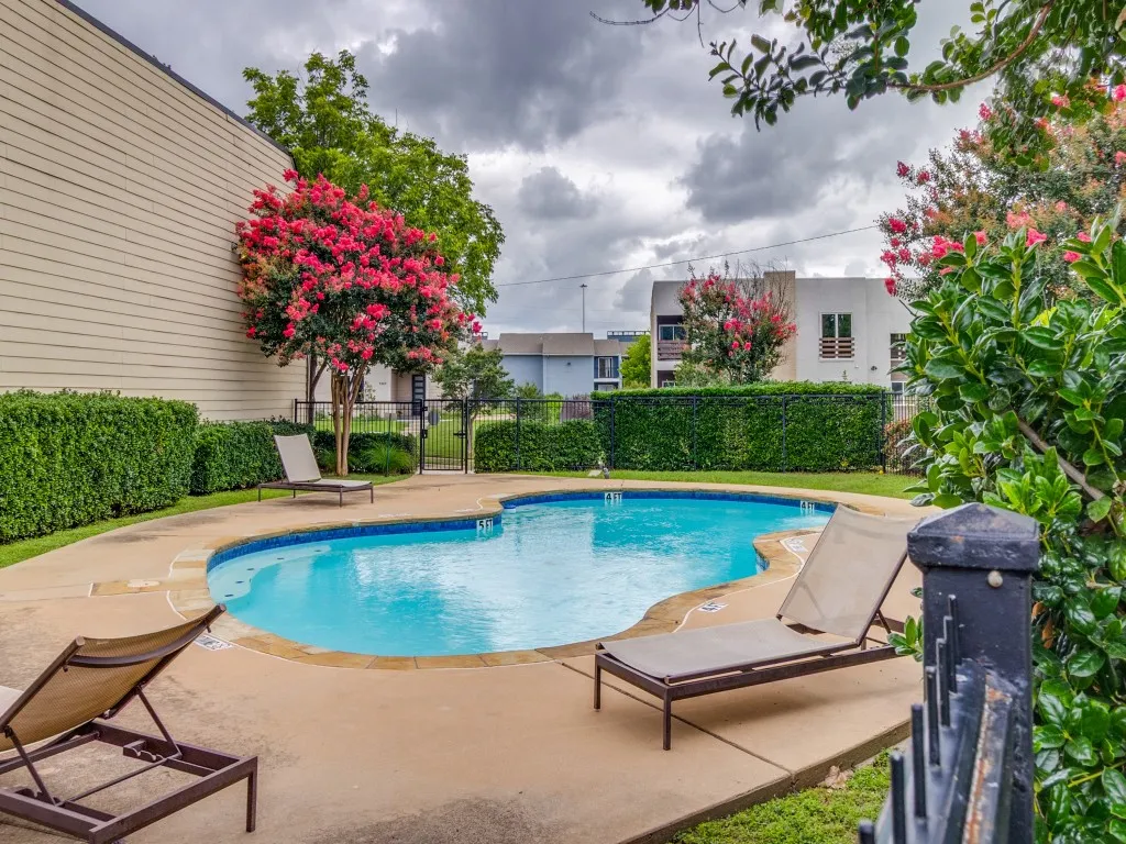 Freeform swimming pool with concrete patio and shaded pergola.