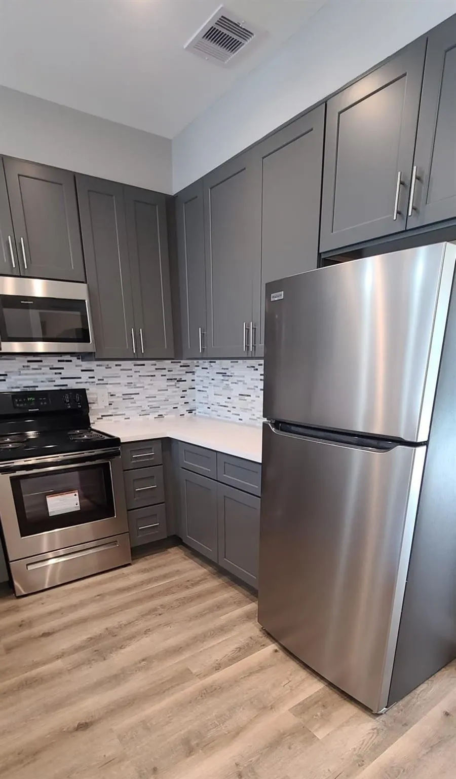 Modern kitchen featuring gray shaker-style cabinetry, stainless steel appliances, white countertops, and a mosaic tile backsplash