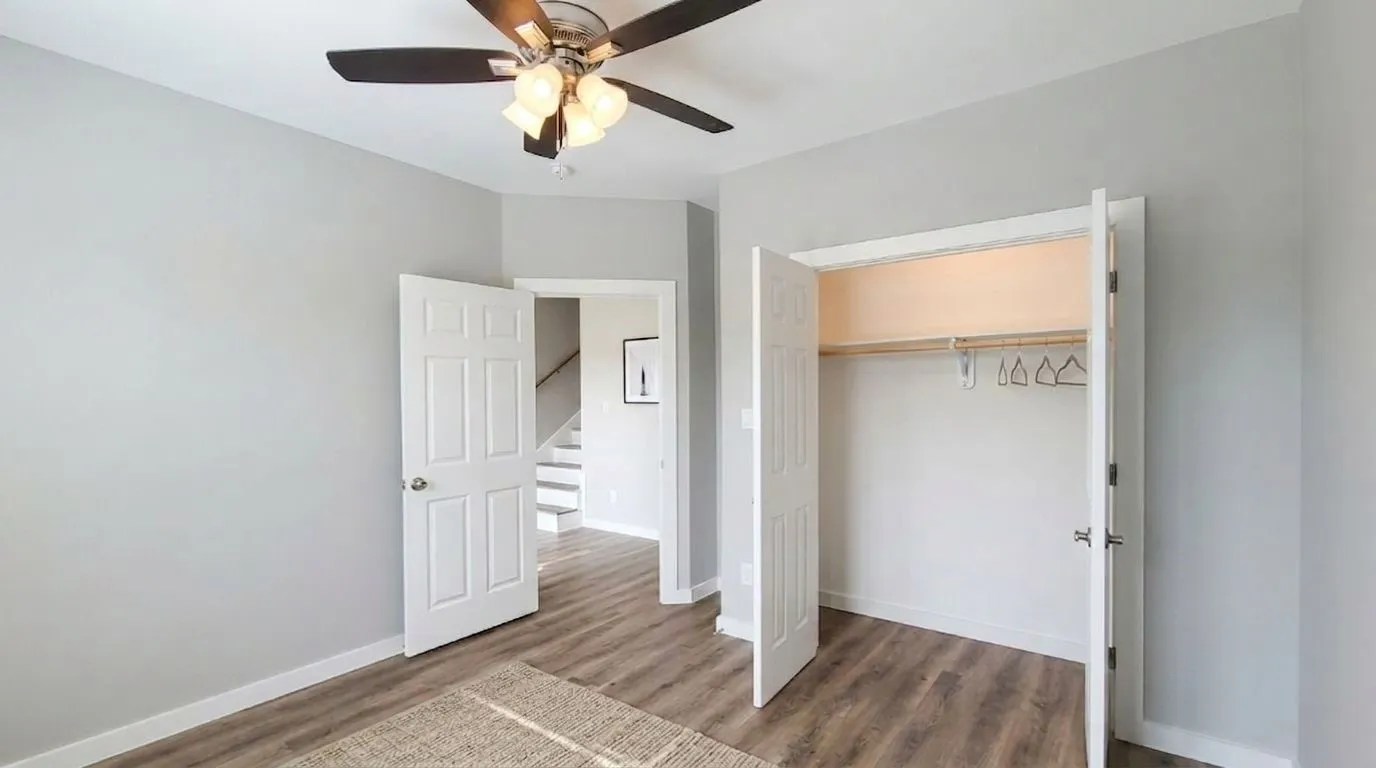 Bedroom 1 - Downstairs Virtually Staged Spacious room featuring vinyl flooring, light gray walls, white trim, a ceiling fan with integrated lighting, and a closet with bifold doors